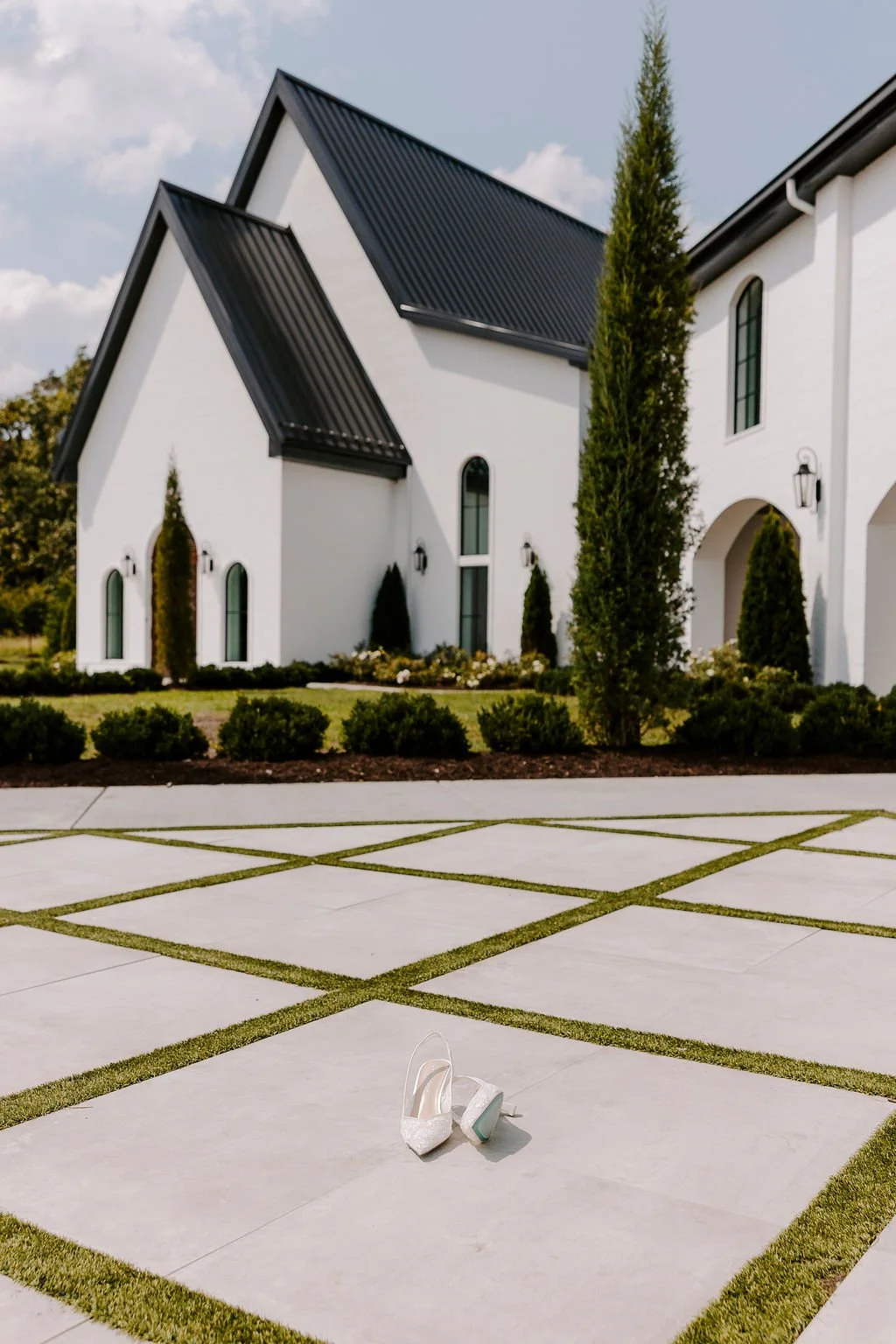 The Grand Wedding Venue Northwest Arkansas modern white chapel with black roof and bridal shoes on courtyard.