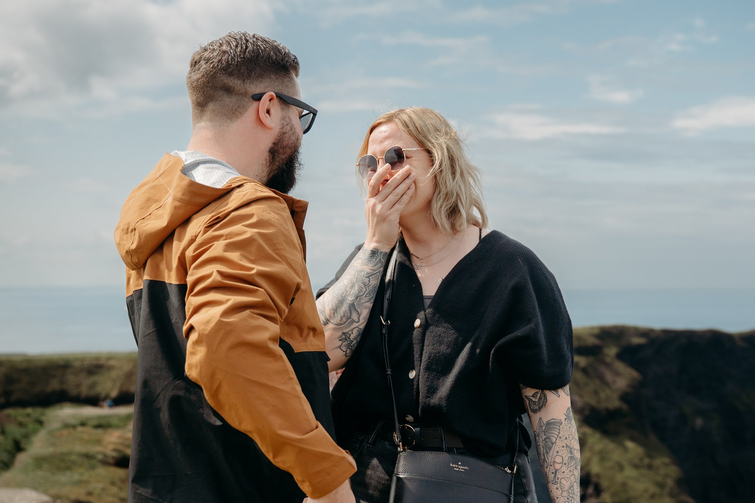 woman covers mouth after proposal at cliffs of mother on a sunny day photographer Marie O'Mahony photography