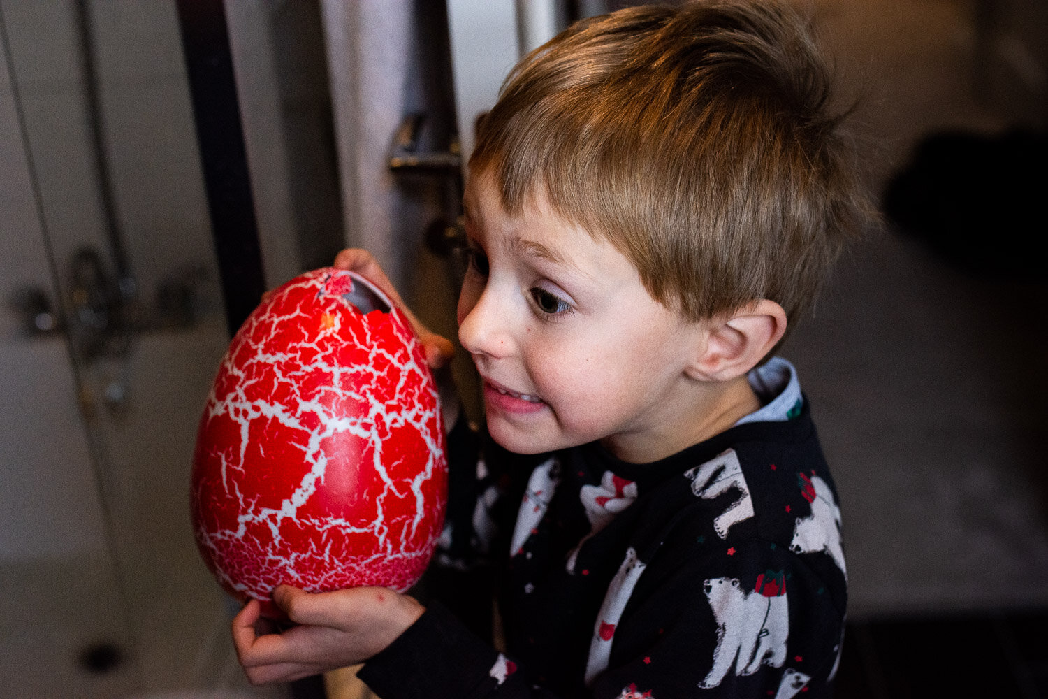 boy in Christmas pajamas holding red dinosaur egg