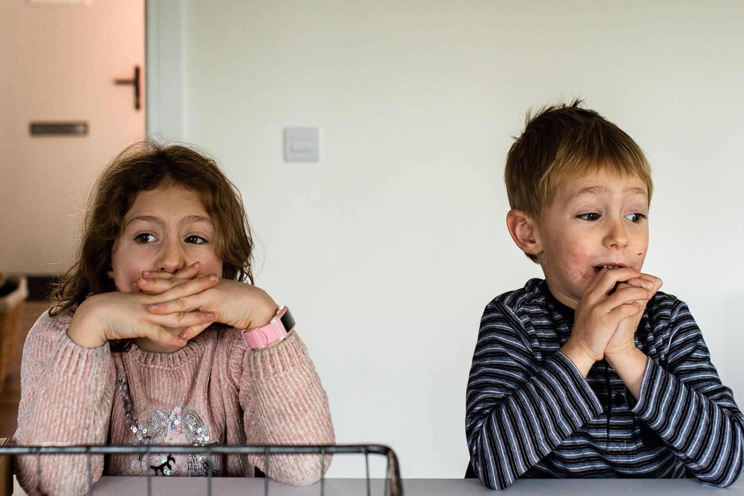 two children in kitchen sitting with hands on faces looking surprised 