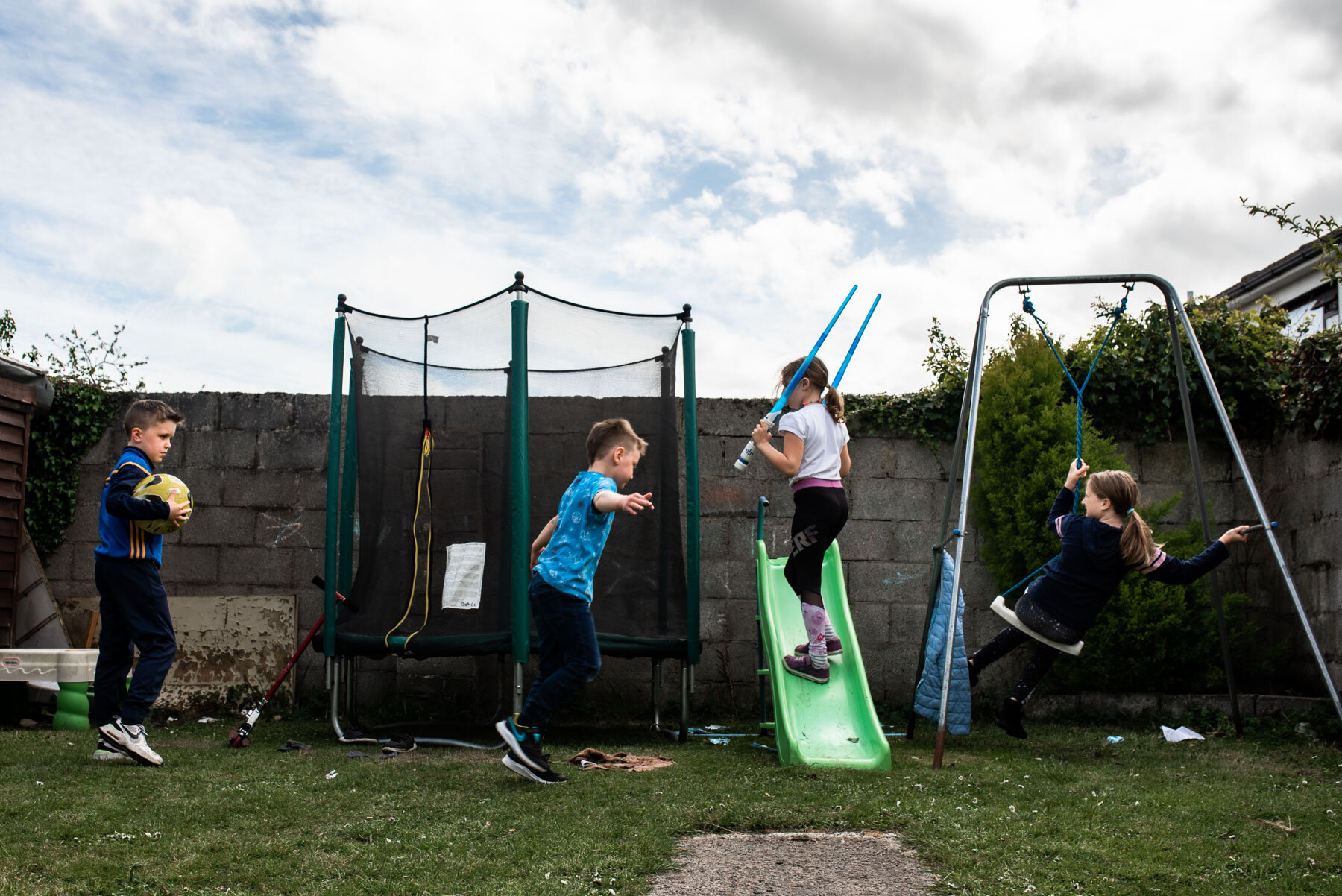 four kids playing in back garden with trampoline, swing and slide at birthday party