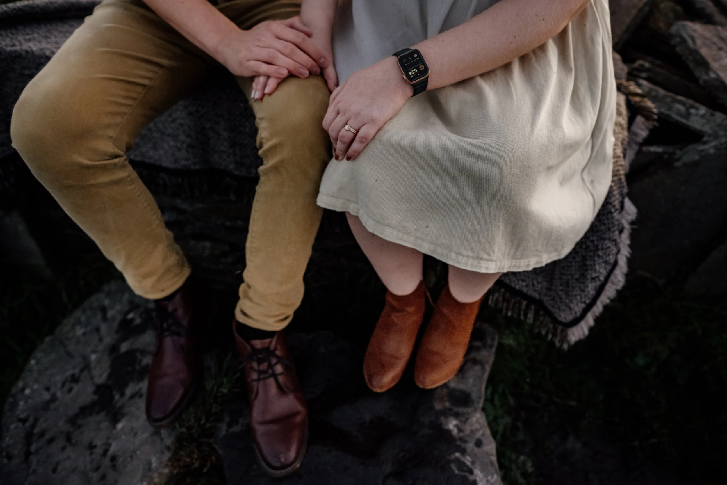 couple holding hands sitting on rock wall at the Cliffs of Moher