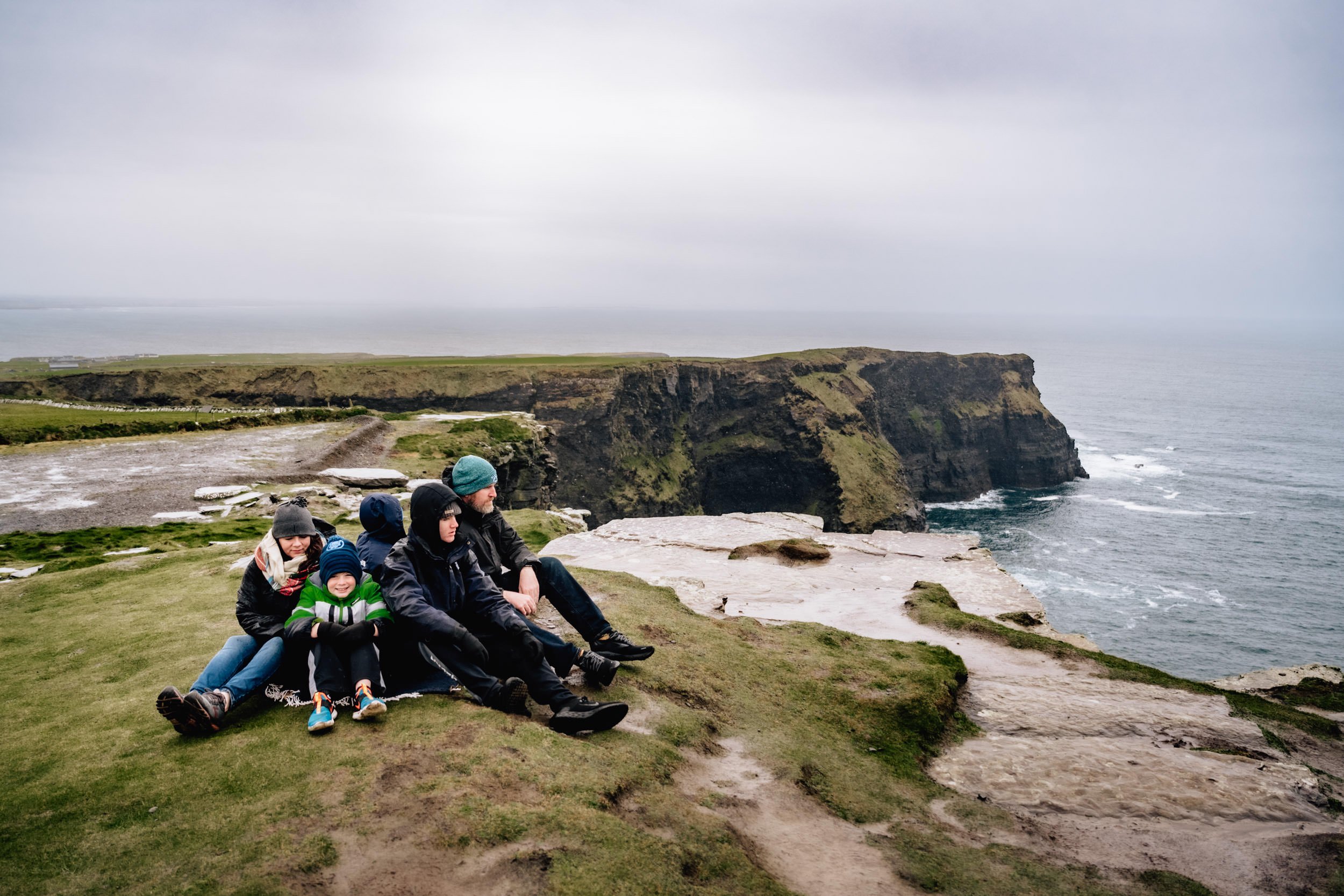 family sitting on cliffs edge at Hags Head Cliffs of Moher Liscannor Co Clare Ireland family photo session