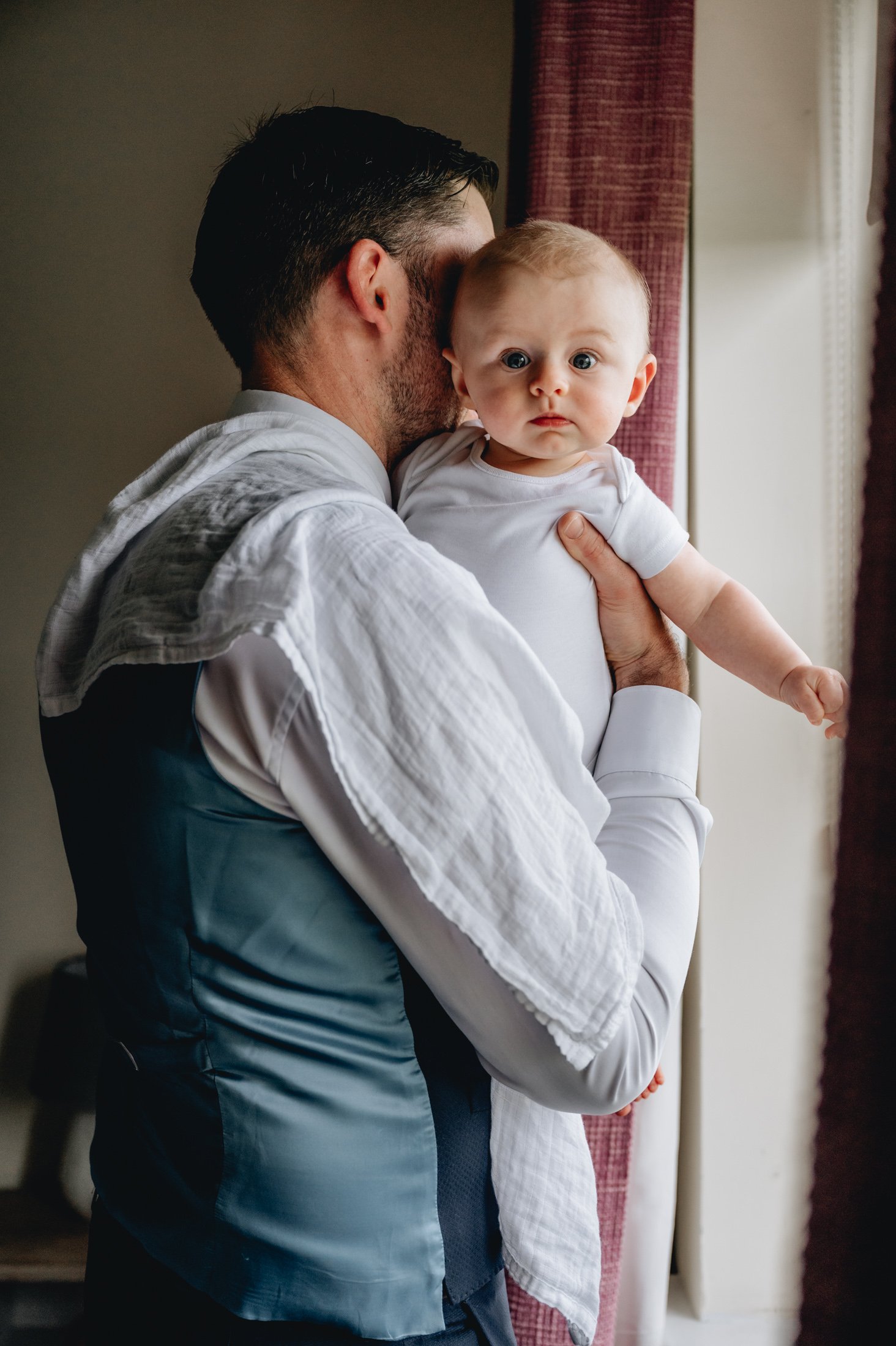 man with burp cloth holding baby boy near window in home family photo christening photos limerick photographer
