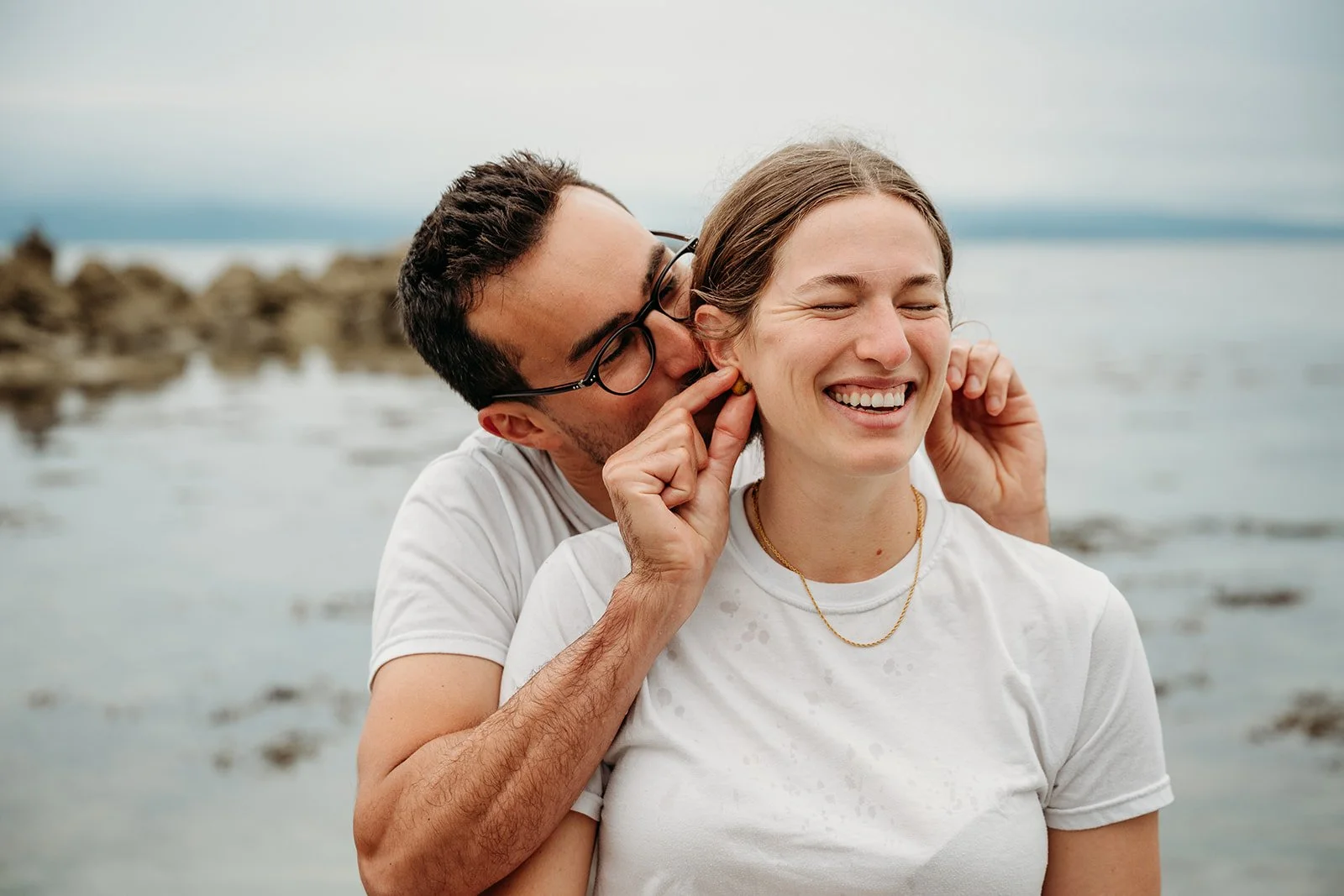 Galway Bay Hotel wedding photos Salthill promenade beach man pretending shells are earrings for woman. Both wearing white t-shirts