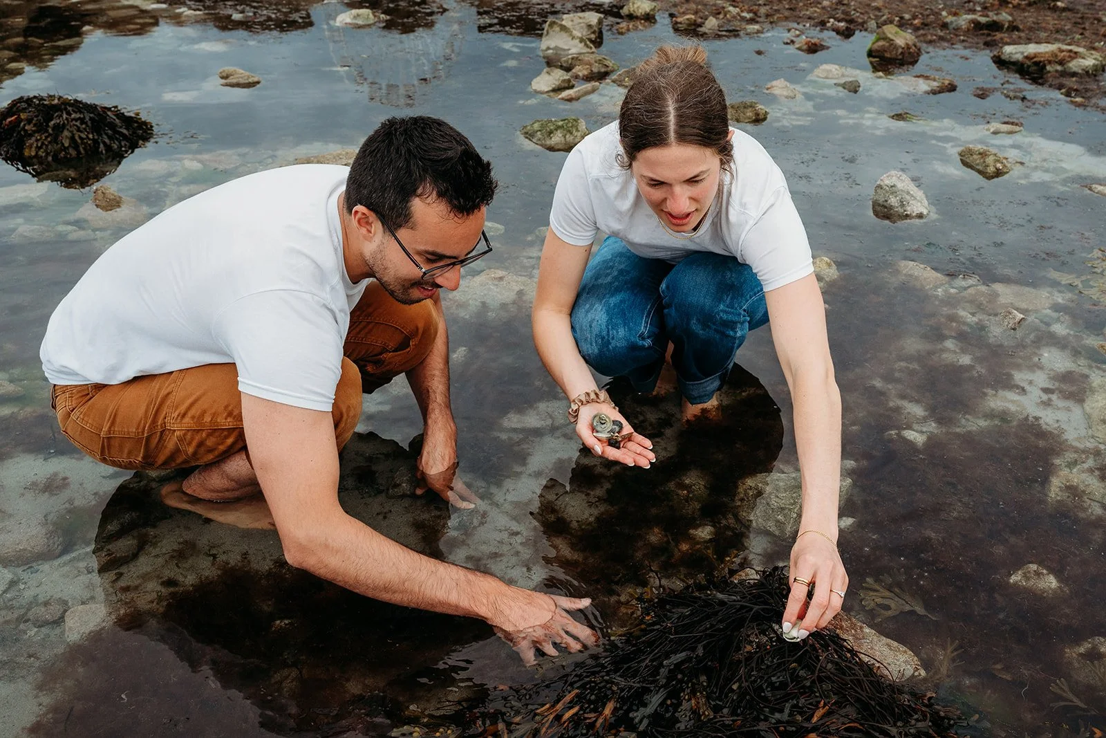 Galway Bay Hotel wedding photos Salthill promenade beach couple squatting gathering rocks and seashells in the water
