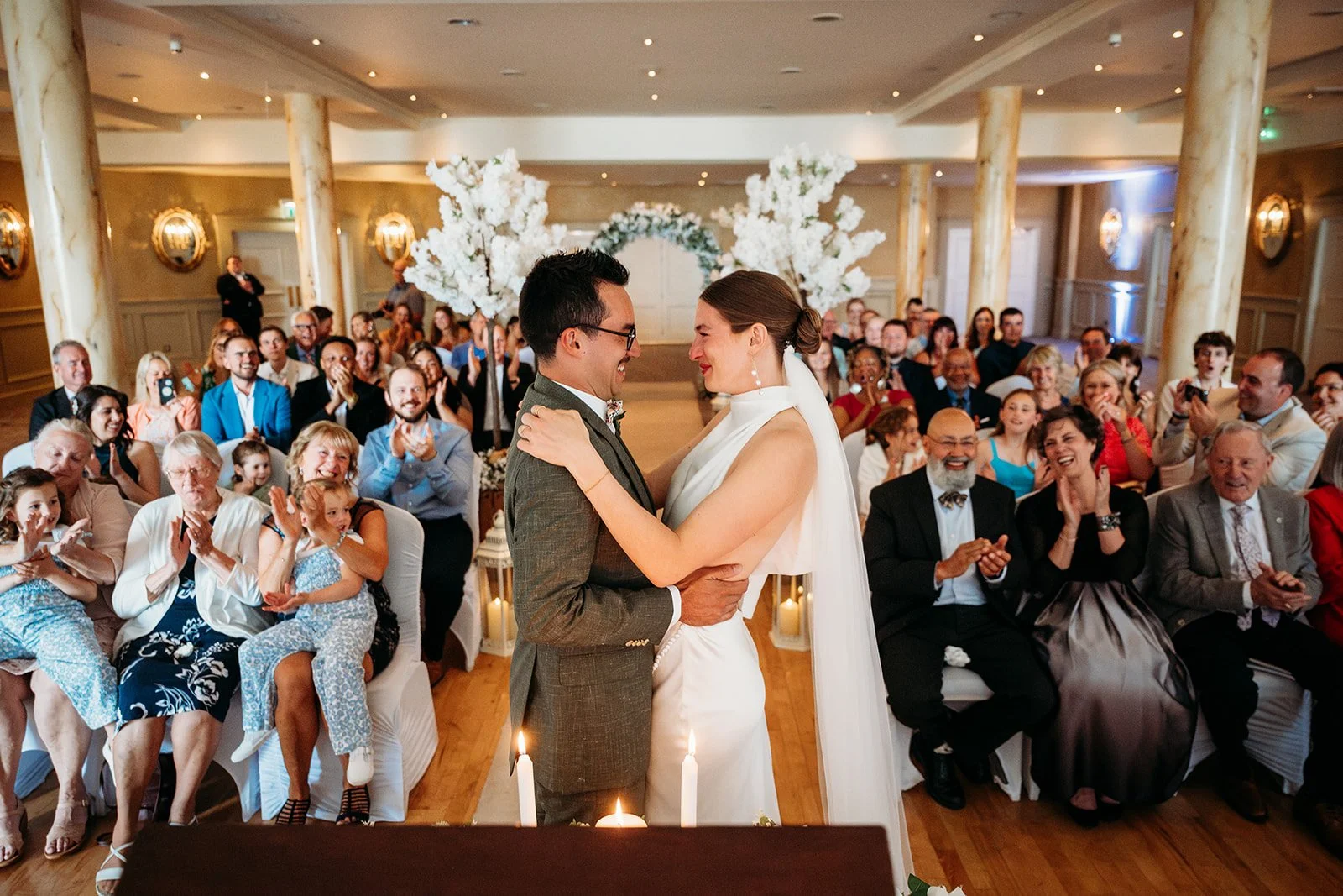 Galway Bay Hotel wedding photos bride and groom grinning while family and friends cheer inside ballroom ceremony