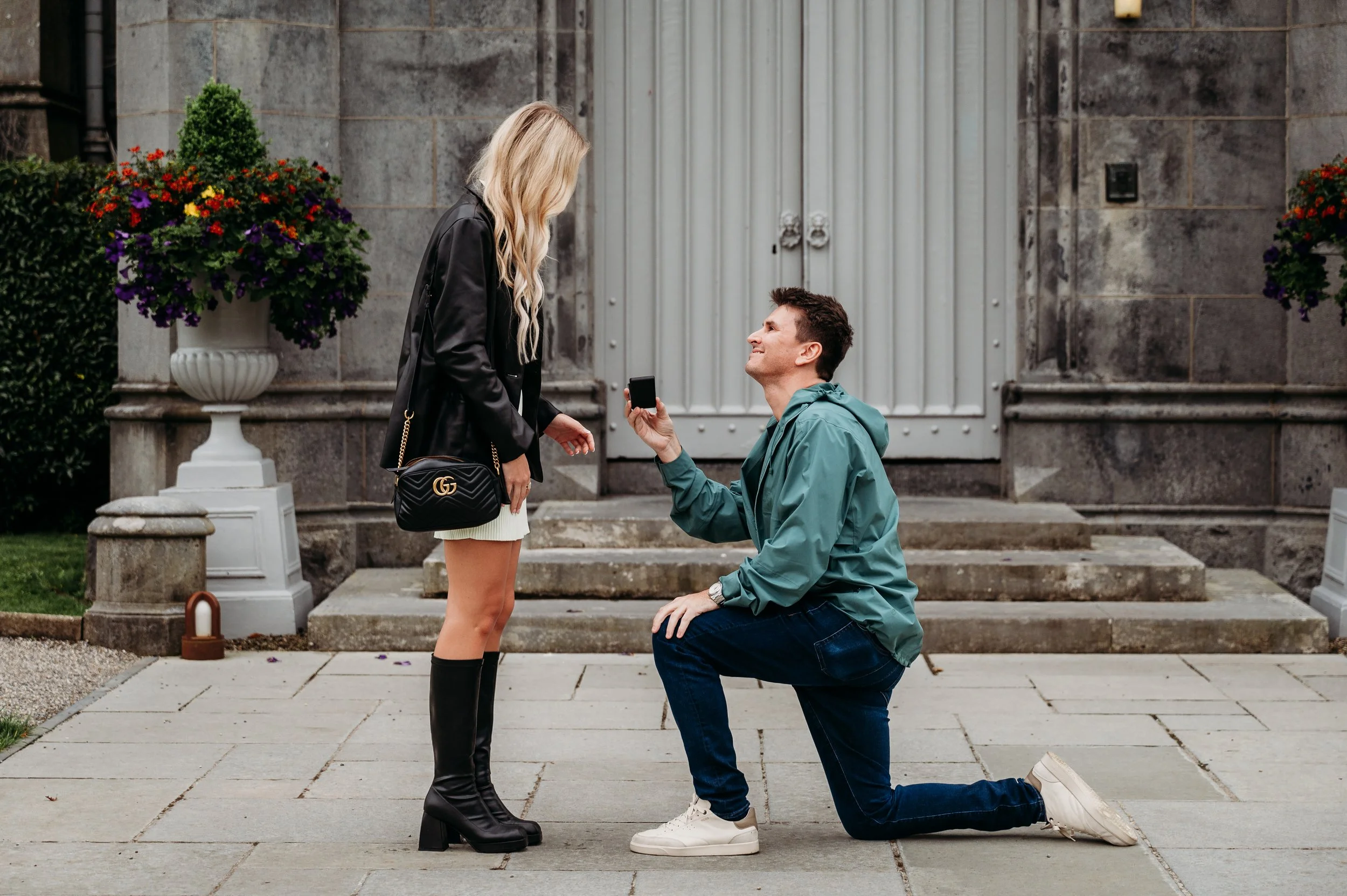 proposal in front of the doors at Dromoland castle, man kneeling holding a ring box and proposing cloudy day couples photographer Ireland Co Clare and Limerick