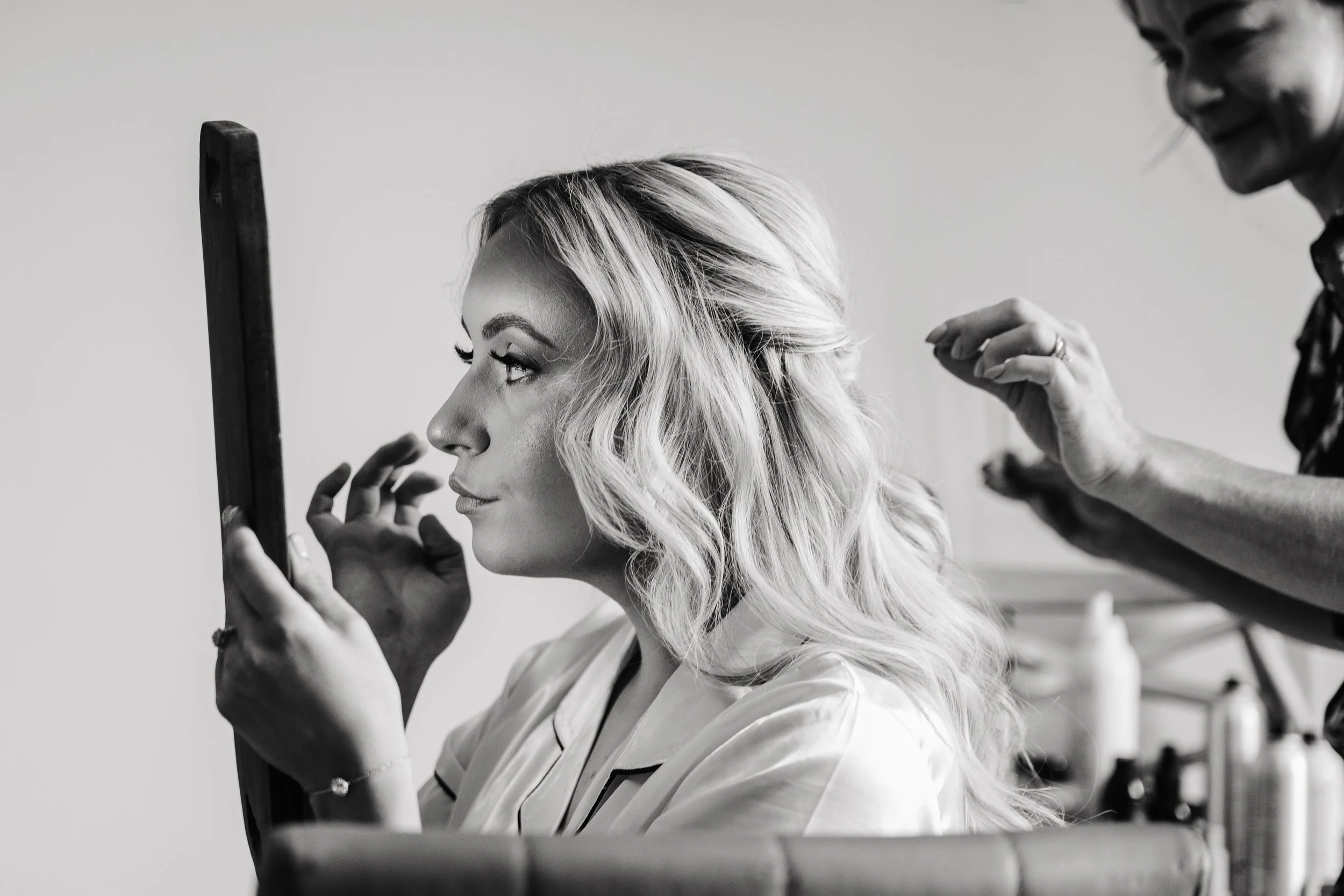 bride looking in mirror while hair stylist works on hair black and white wedding photo natural candid moment reportage ireland