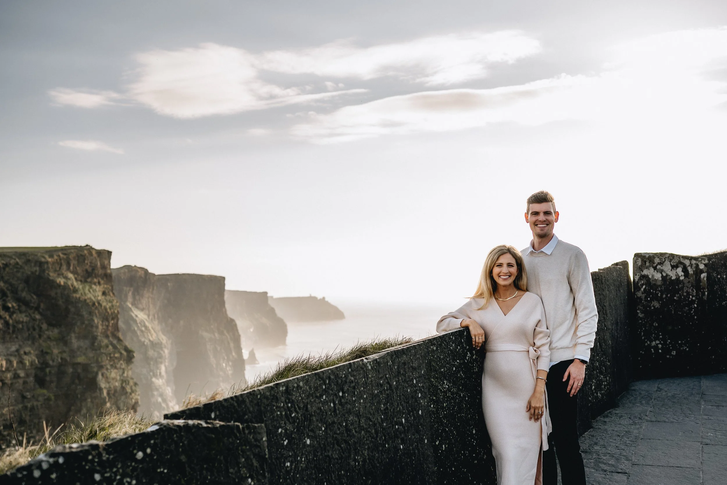 Cliffs of moher photo session maternity photos co clare woman in cream dress and man in cream shirt looking at camera and smiling cliffs in the distance 