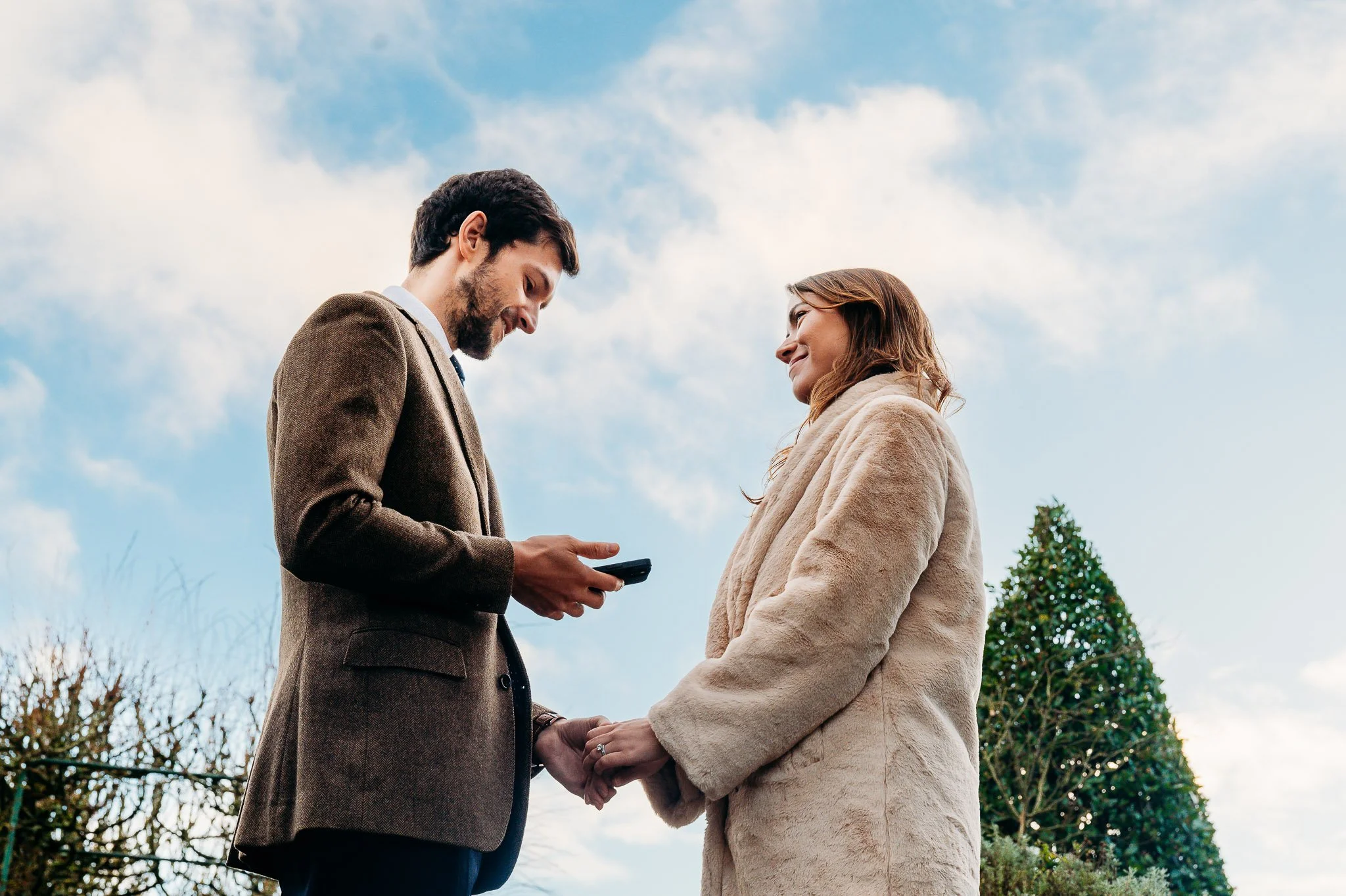 man reading vows on phone to woman against blue sky vow renewal ceremony