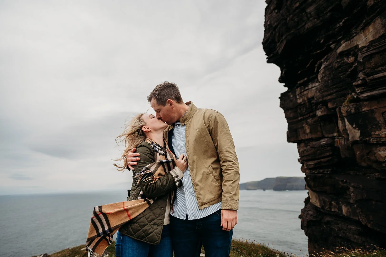 Surprise proposal Cliffs of Moher proposal photographer in Ireland couple kissing cliffs in the background grey sky autumn