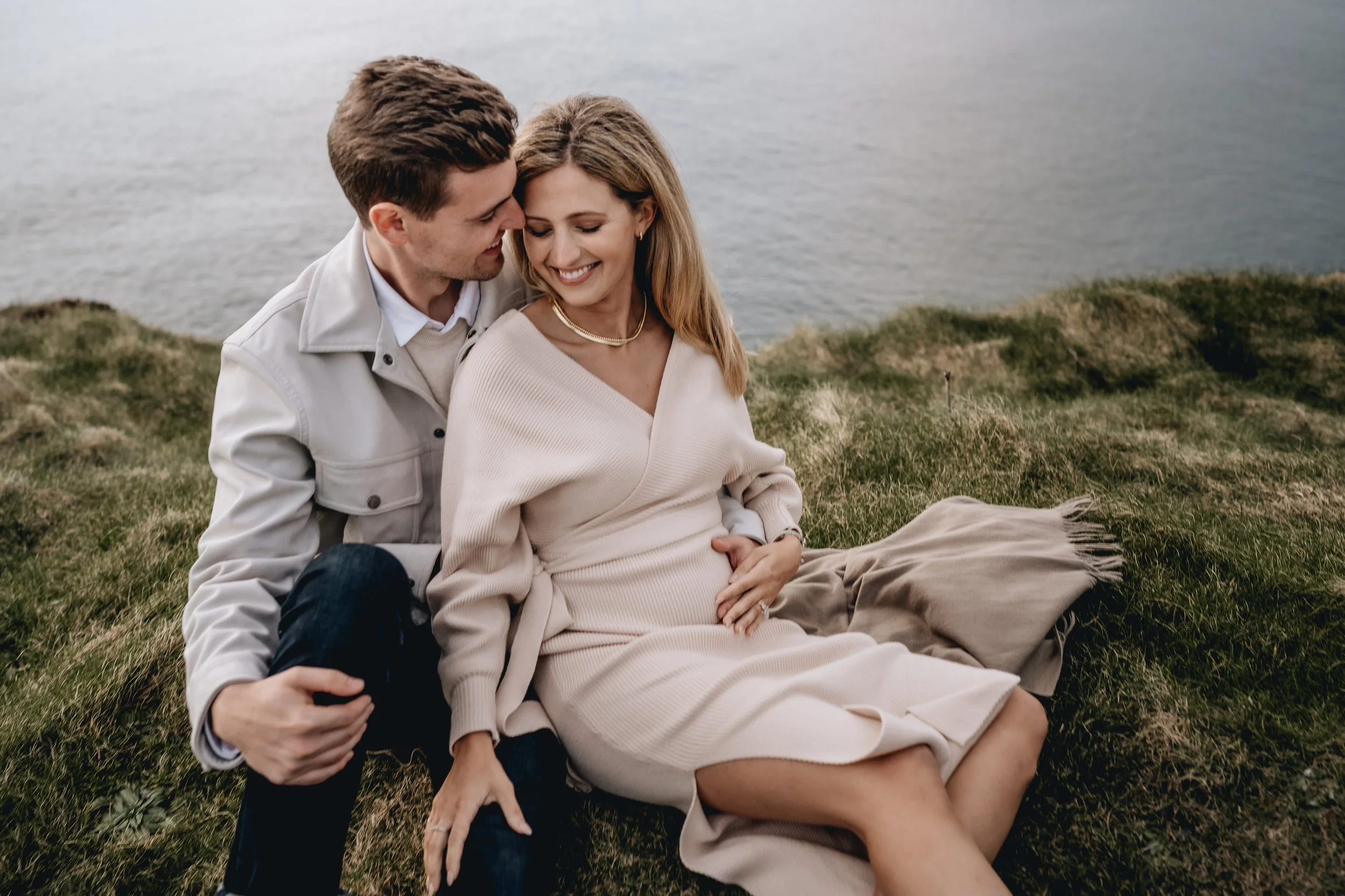 Couple sitting on cliff edge Liscannor Cliffs of Moher maternity photo session photographer Ireland