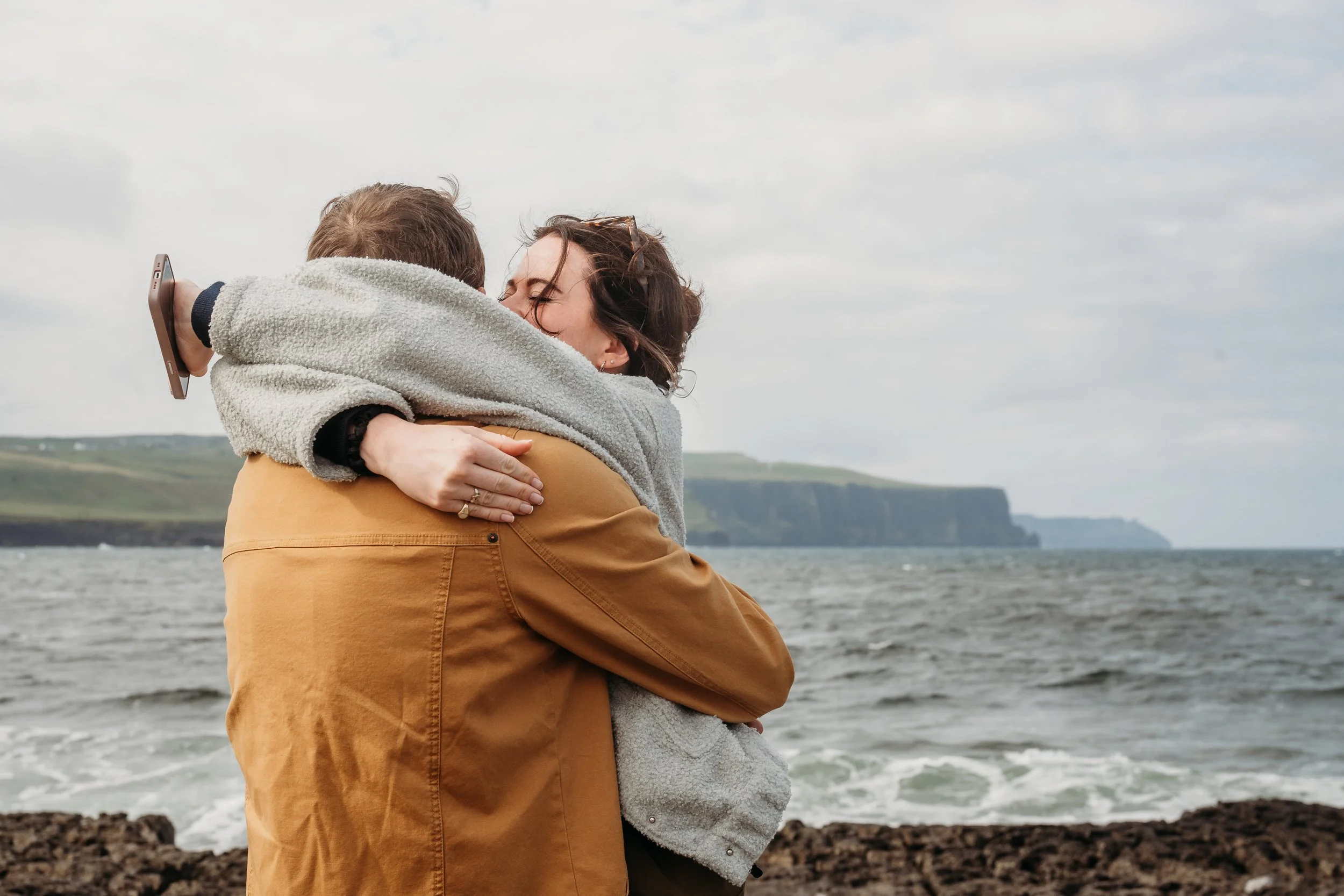 woman gives big hug after suprise proposal Doolin pier cliffs of mother in the background winter clothes