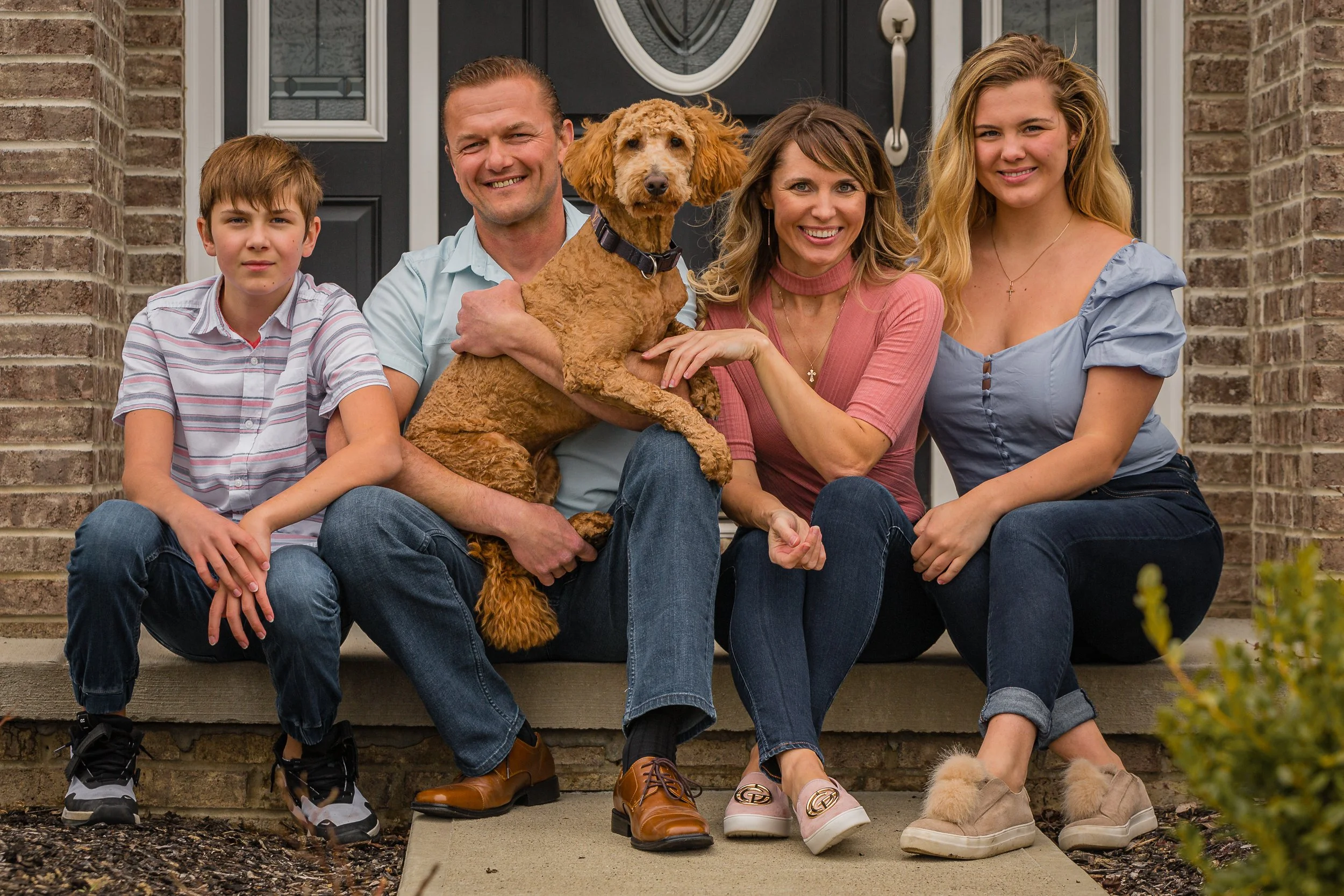 Family sitting on front porch steps with their dog, smiling at the camera.