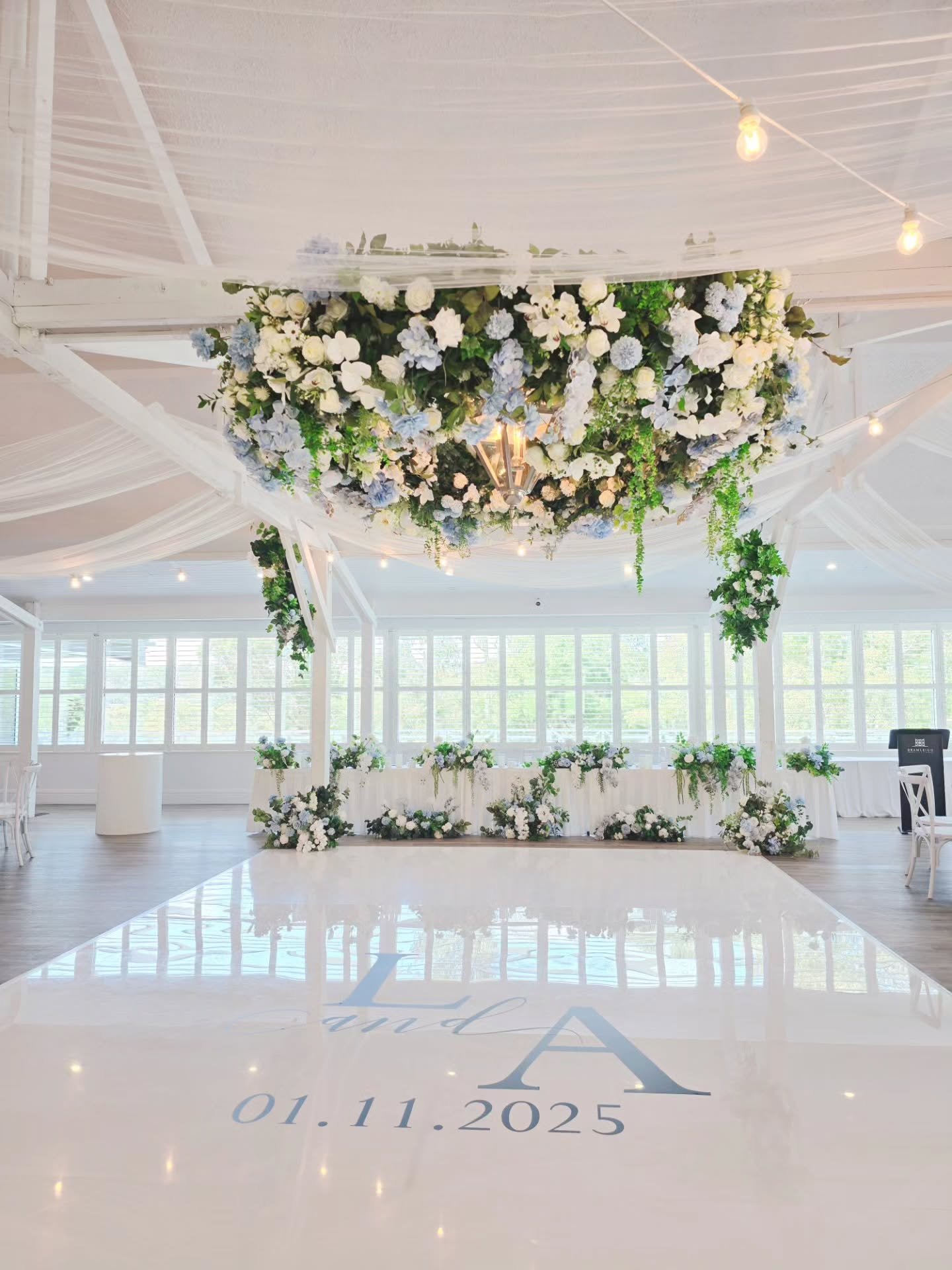✨ A timeless garden romance ✨
Featuring sheer draping on the ceiling, serene white and blue tones, and lush cascading florals that set the scene for pure elegance.

Soft drapes, delicate blooms, and the glow of a glossy white dance floor &mdash; a fr