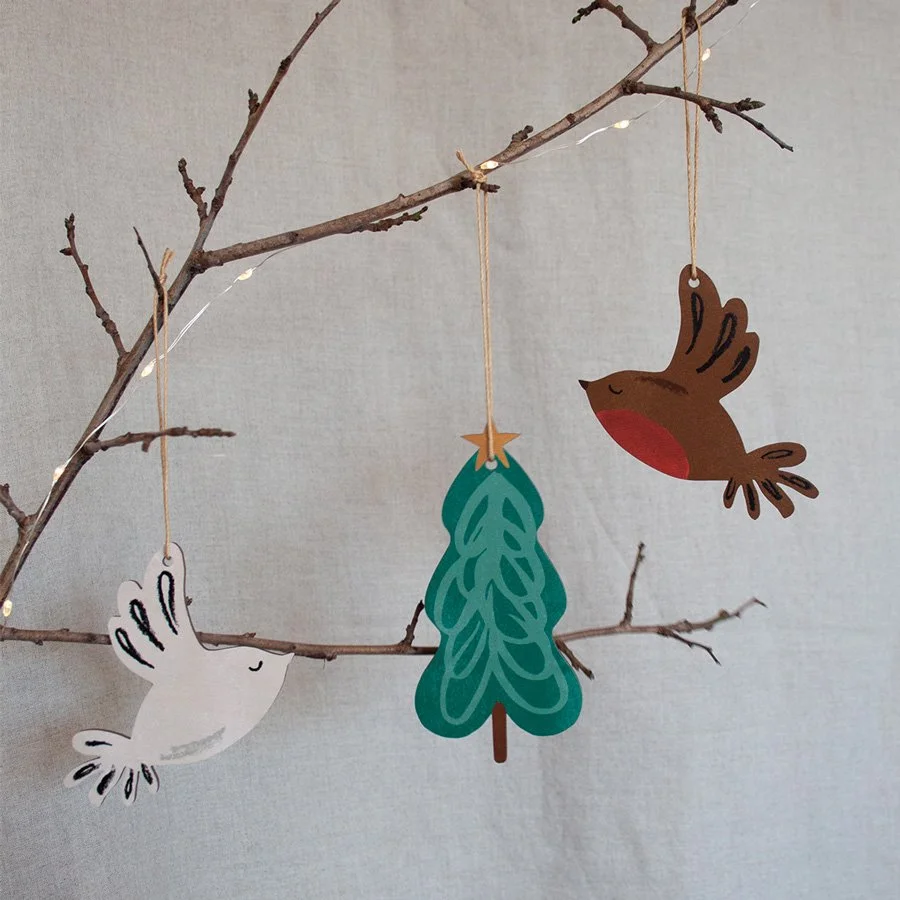 Wooden Christmas decorations hanging from a natural branch with linen background and lights