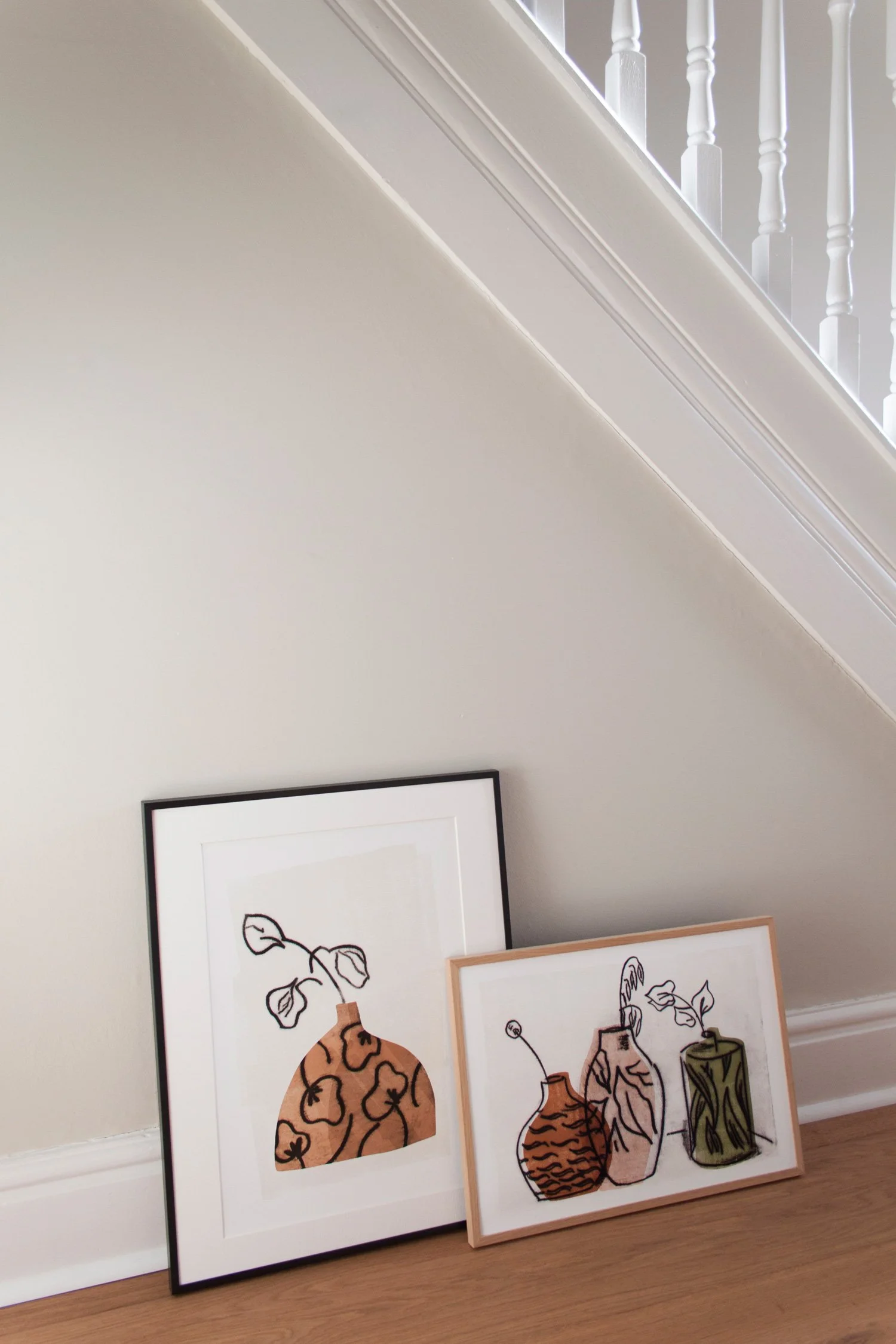Two vase art prints leant up against a neutral wall in a hallway