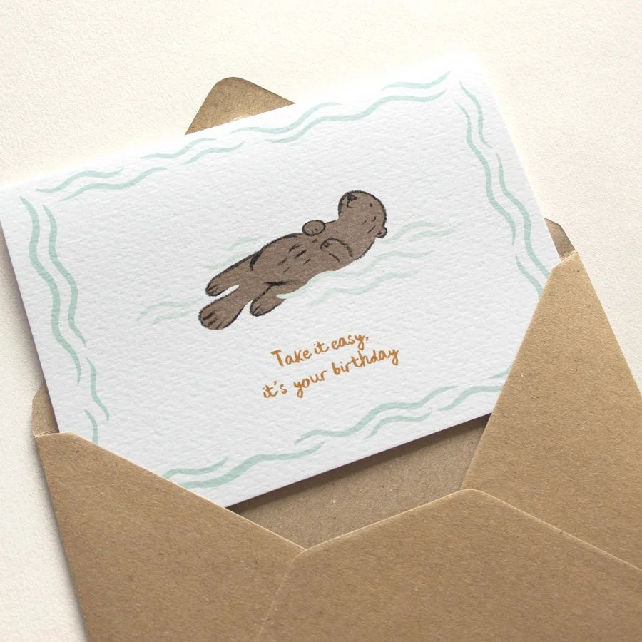 Otter birthday card in kraft envelope on plain background