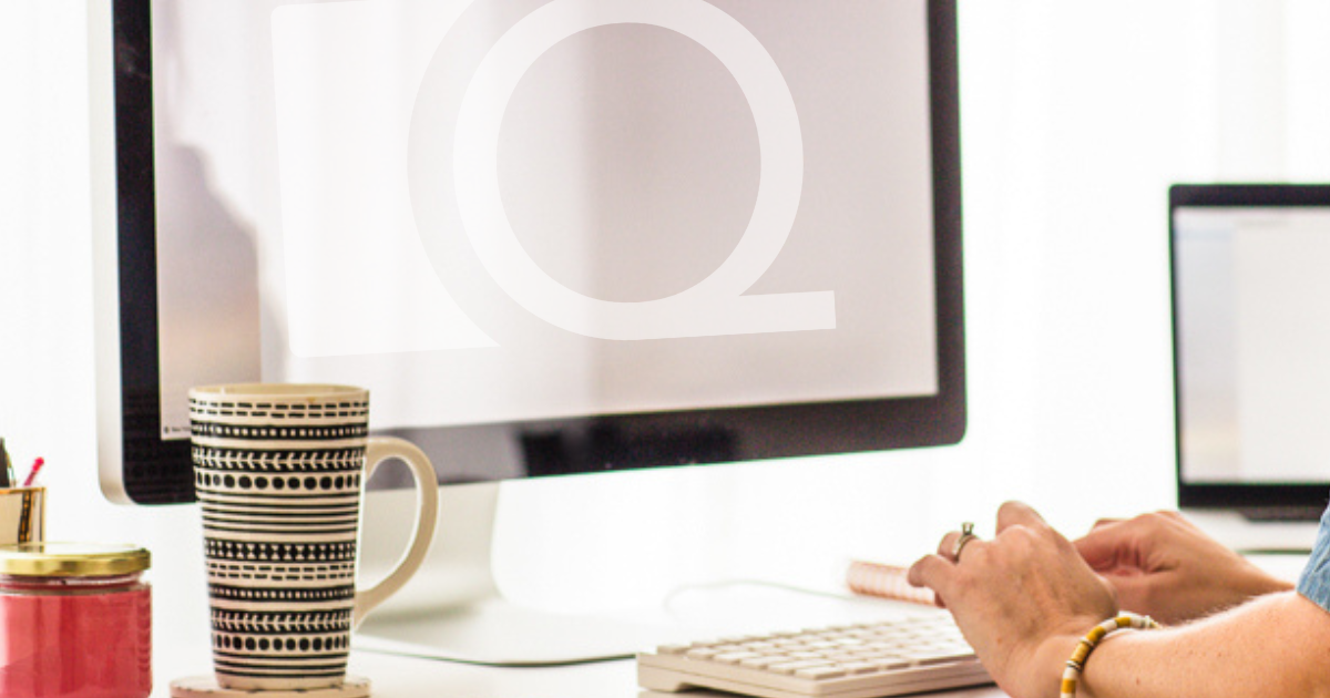 A person working at a desk with a computer, mug with black and white patterns, and a pink container, in a bright office environment.