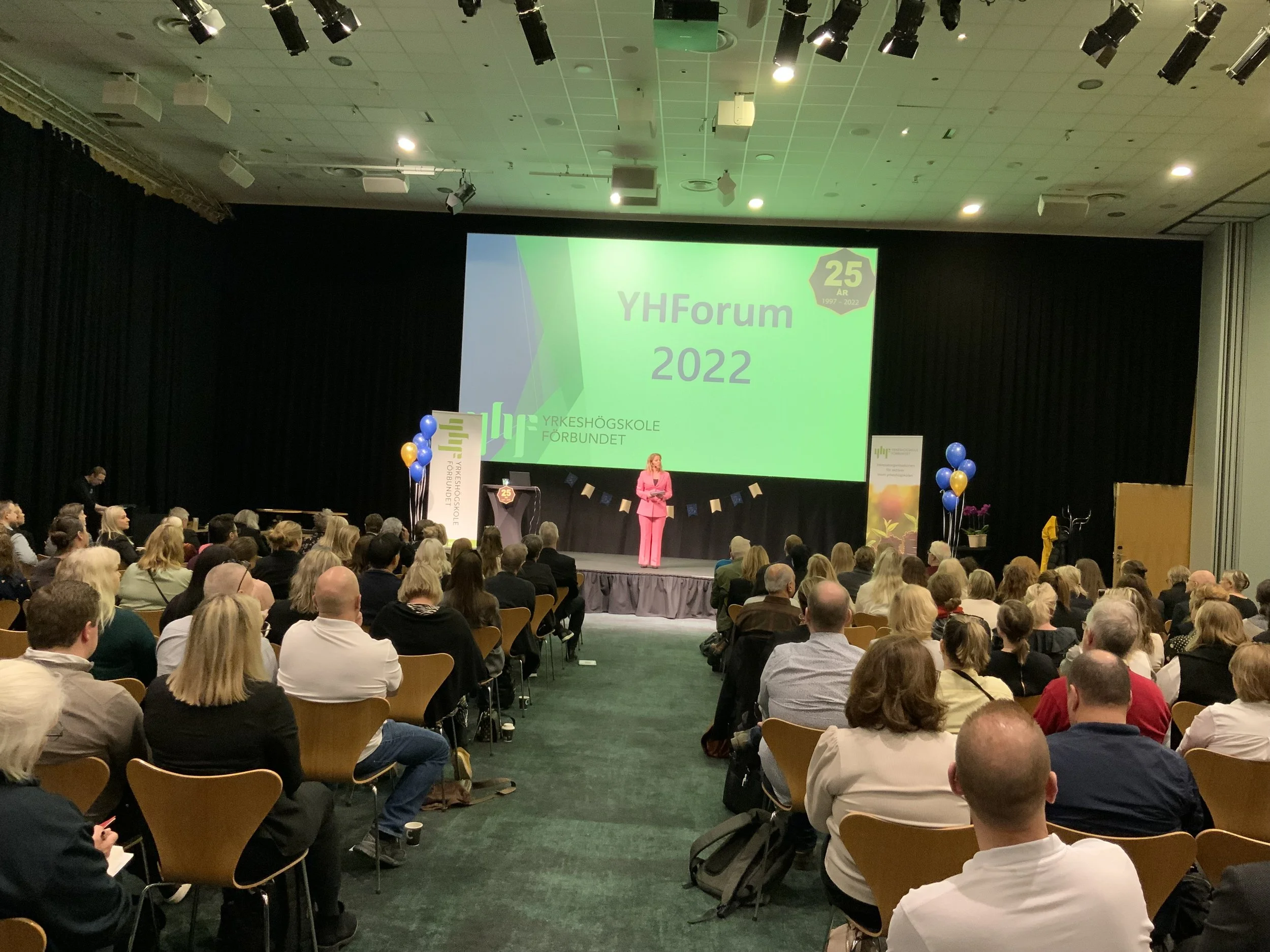 Sanna Balsvik moderator på scenen under YH Forum, i rosa kostym