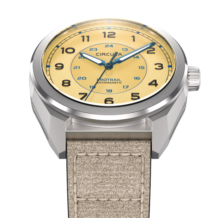 Close-up of a wristwatch with a beige dial, black Arabic numerals, and a beige fabric strap.