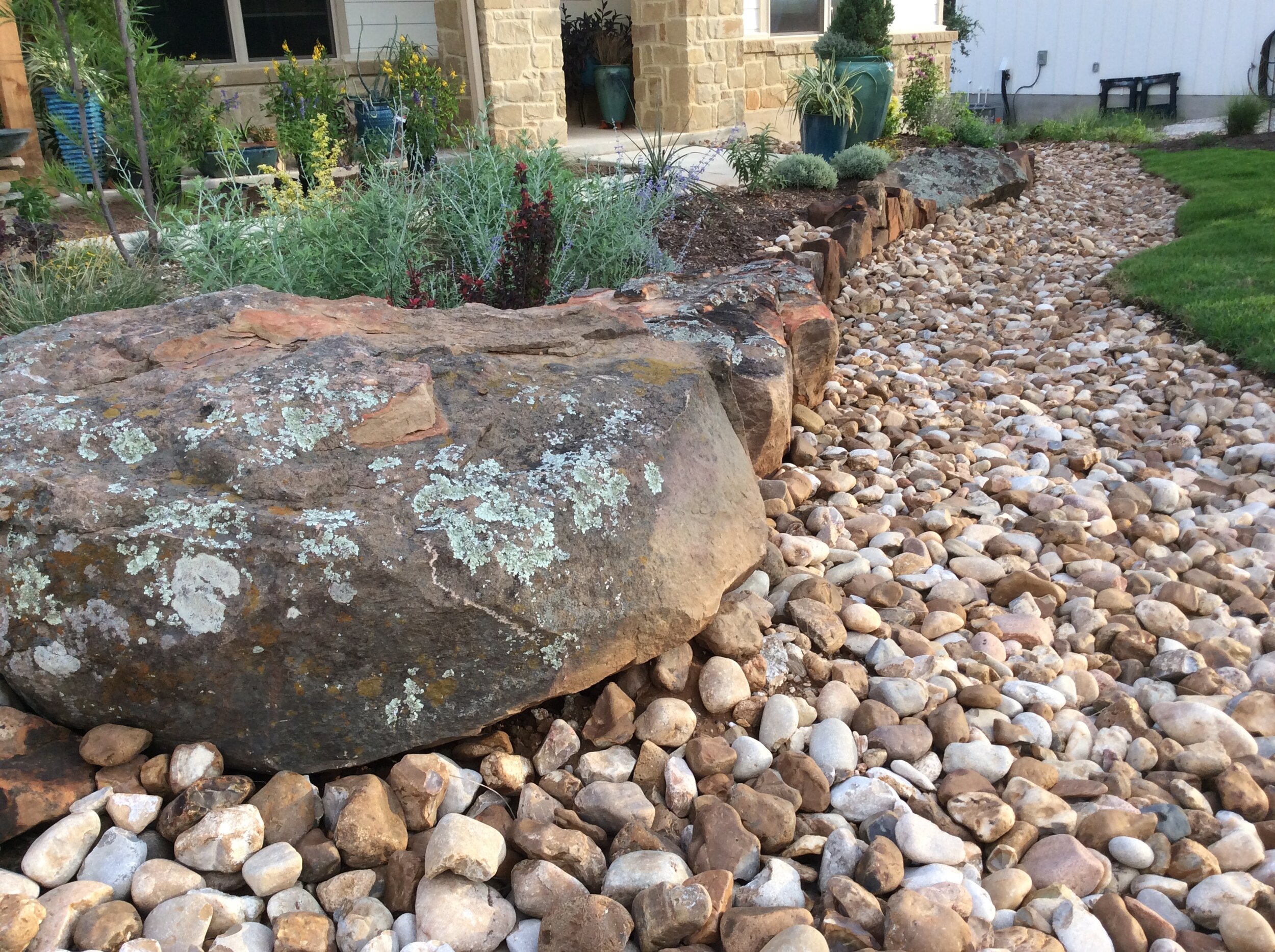 River rock dry creek with moss rock retaining wall, raised planting beds &amp; drought tolerant Zoysia Grass lawn installation.