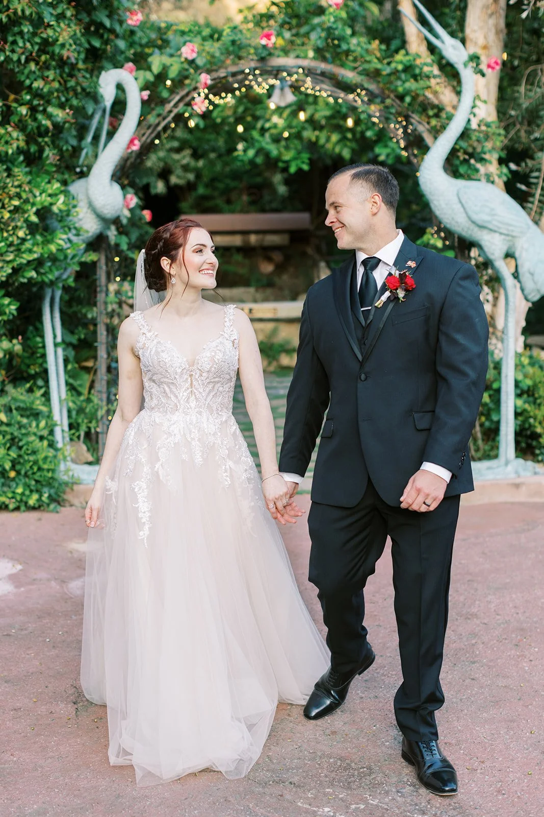 Bride and groom walking side by side, gazing at each other between tall bird statues at the Houdini Estate