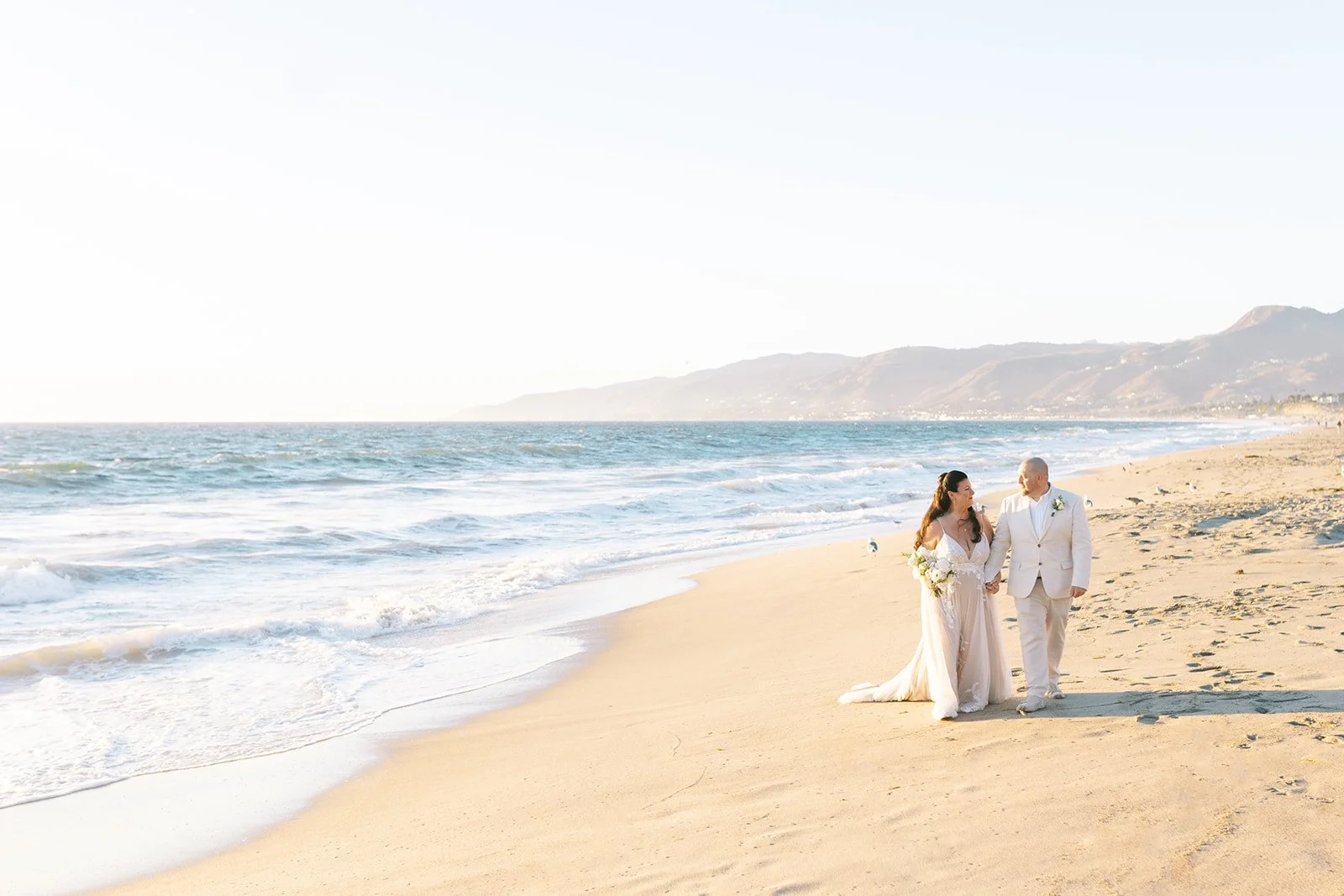 Newlywed couple walking hand in hand on the beach at sunset during their Point Dume elopement in Malibu