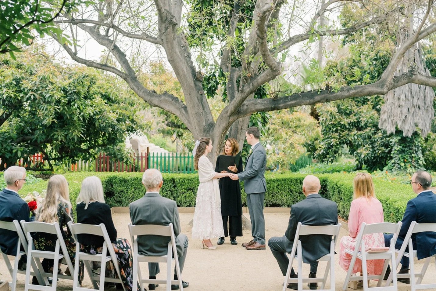 Couple standing with their officiant as guests look on during their elopement ceremony at the Fullerton Arboretum