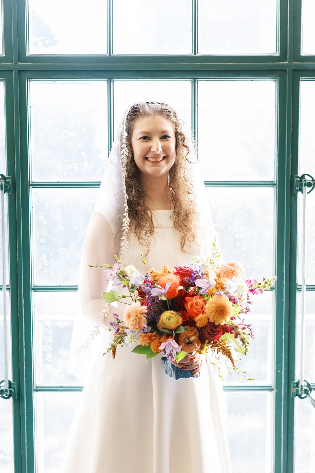 Portrait of the bride holding her bouquet in front of the tall windows of the Los Angeles Central Library