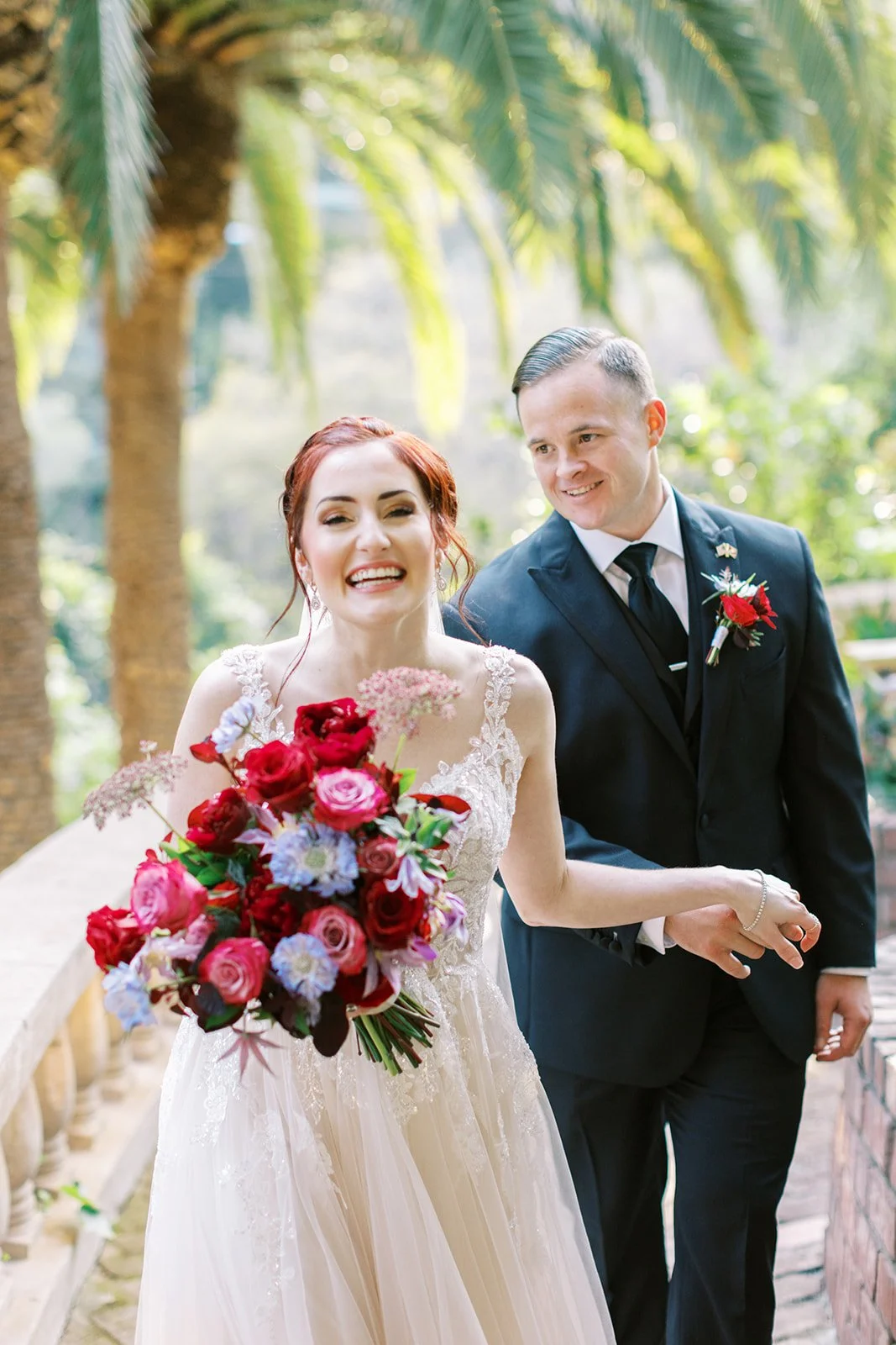 Smiling bride with her bouquet, groom gazing at her from behind, at their Los Angeles elopement