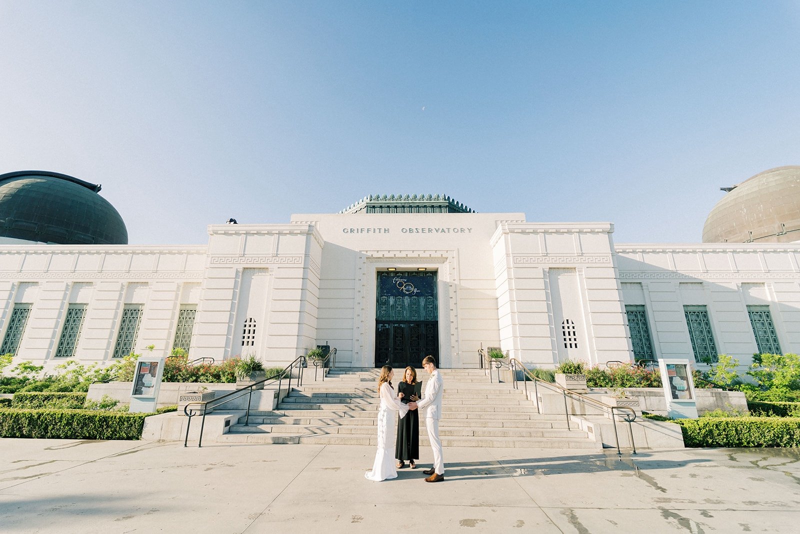 Couple exchanging vows with their officiant in front of Griffith Observatory at sunrise.
