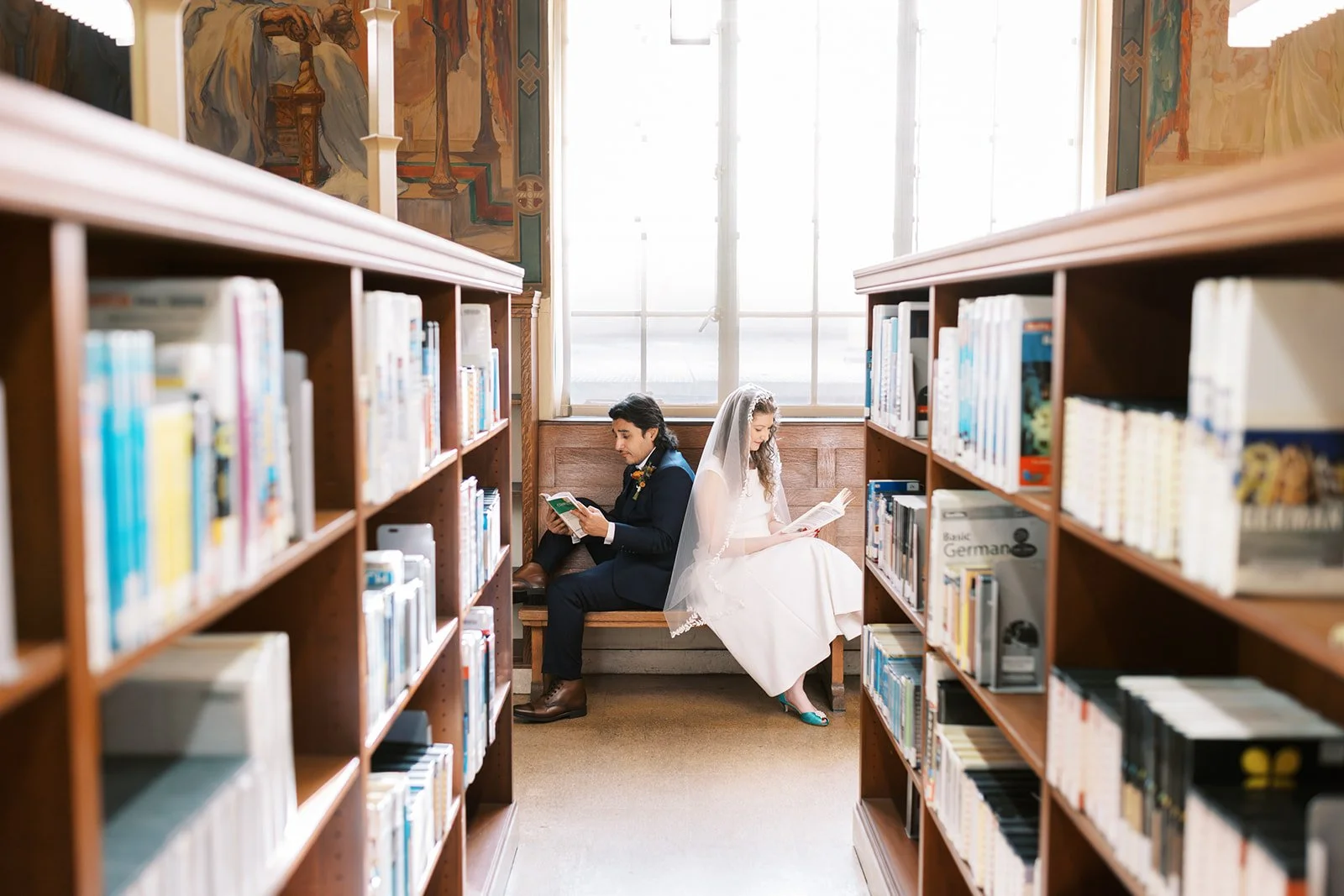 Bride and groom sitting back to back on a bench, each reading a book, at the Los Angeles Central Library
