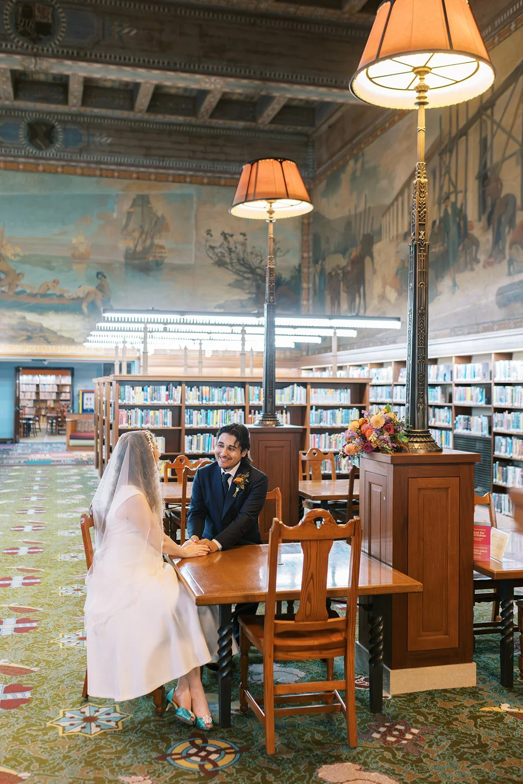Bride and groom holding hands across a table in the reading room of the Los Angeles Central Library