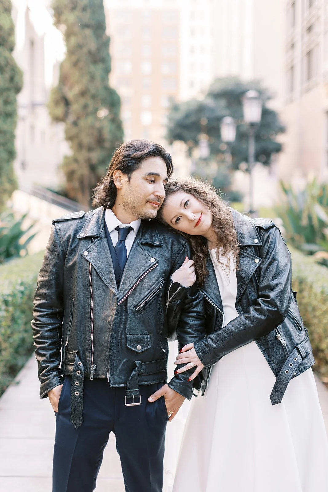 Bride and groom in matching leather jackets, holding hands as she rests her head on his shoulder