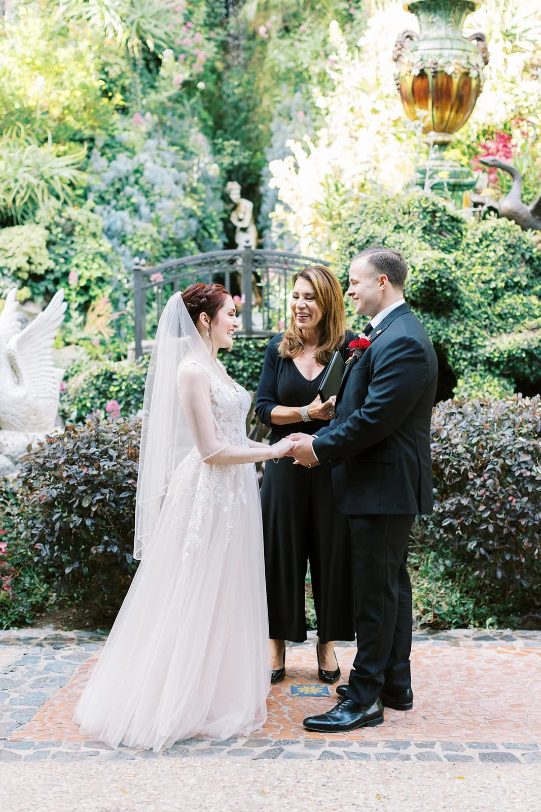 Bride and groom exchanging vows among the statues and lush foliage of the Houdini Estate gardens