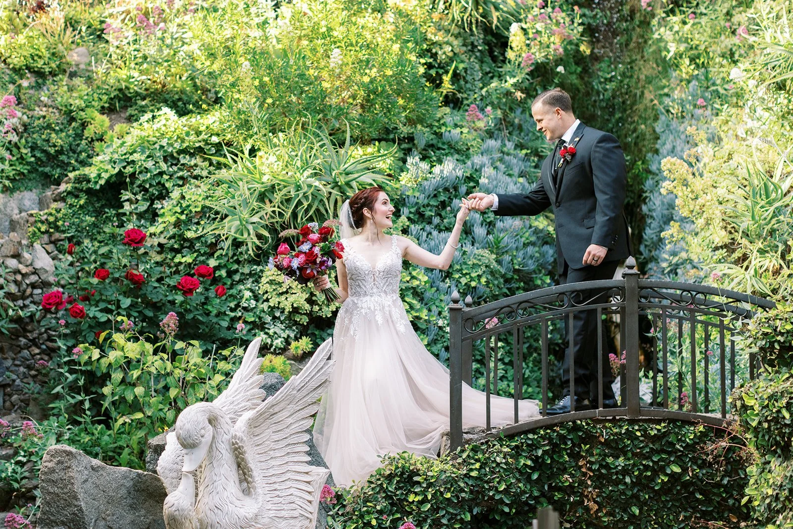 Bride looking back at the groom as they walk hand in hand over a small bridge in the gardens of the Houdini Estate