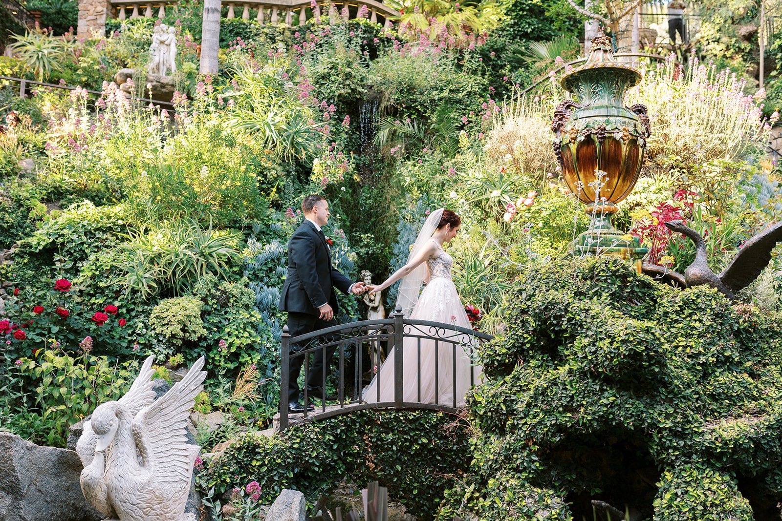 Bride and groom holding hands as they cross a garden bridge at the Houdini Estate, surrounded by greenery
