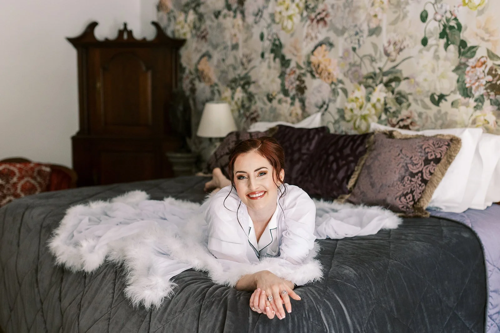 Bride in her robe, makeup finished, posing on the bed before getting dressed for her ceremony