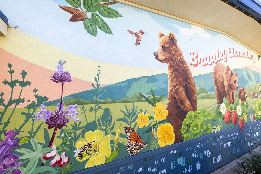Bradley Elementary School Mural featuring grizzly bears, monarch butterflies, honey bees, strawberries, green hills, red apples, blackberries, and other local flowers, creatures, and plants by Brittany Costanzo Creative 2026