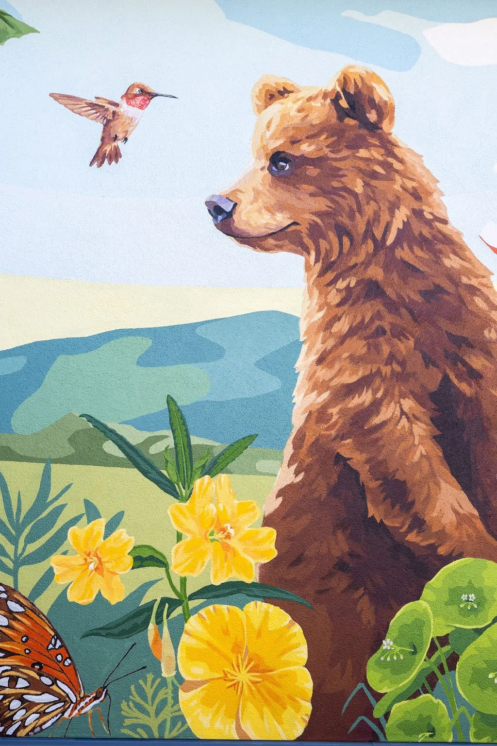 Bradley Elementary School Mural featuring grizzly bears, a humming bird, monarch butterflies, honey bees, strawberries, green hills, red apples, blackberries, and other local flowers, creatures, and plants by Brittany Costanzo Creative 2026