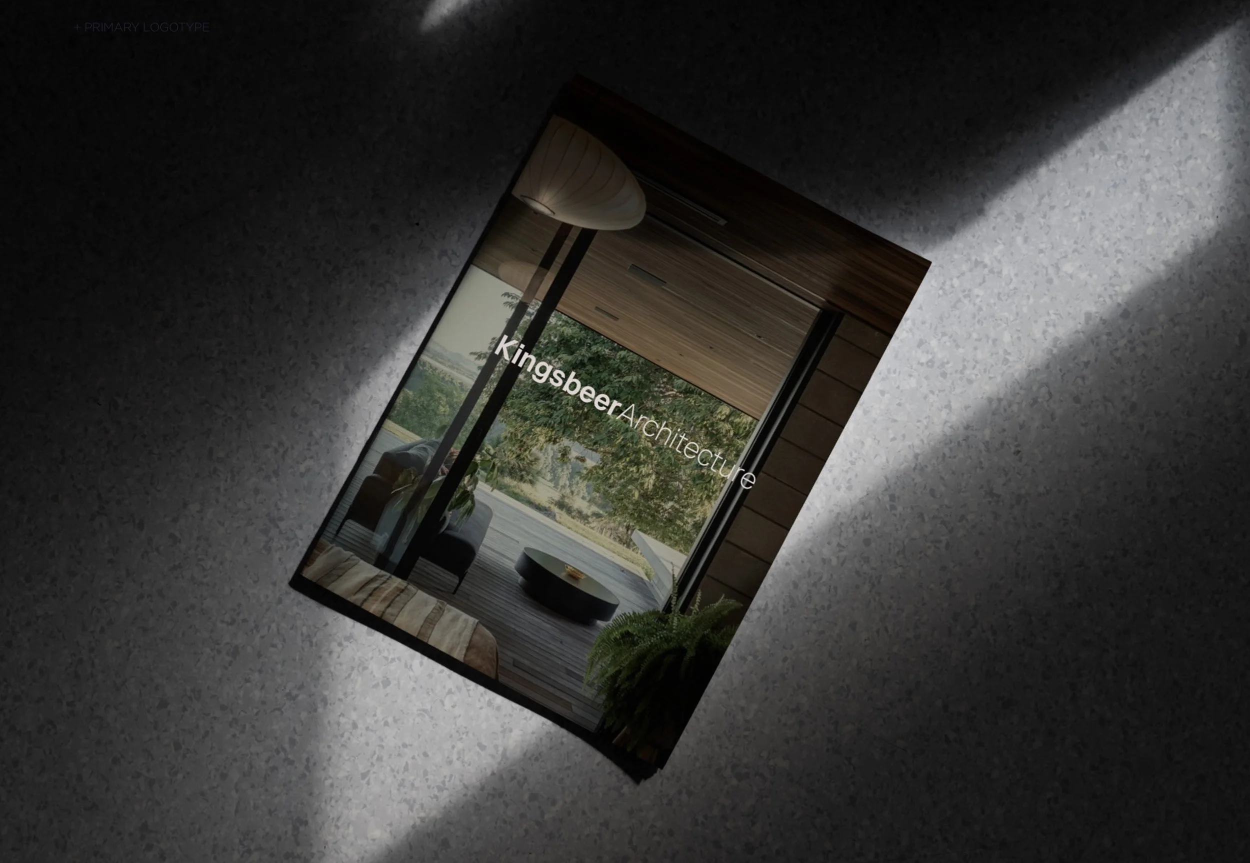 A brochure or magazine with the title 'Kingsbeer Architecture' on a textured gray surface, lit by a beam of light, showing an interior view of a modern room with large windows and outdoor scenery.