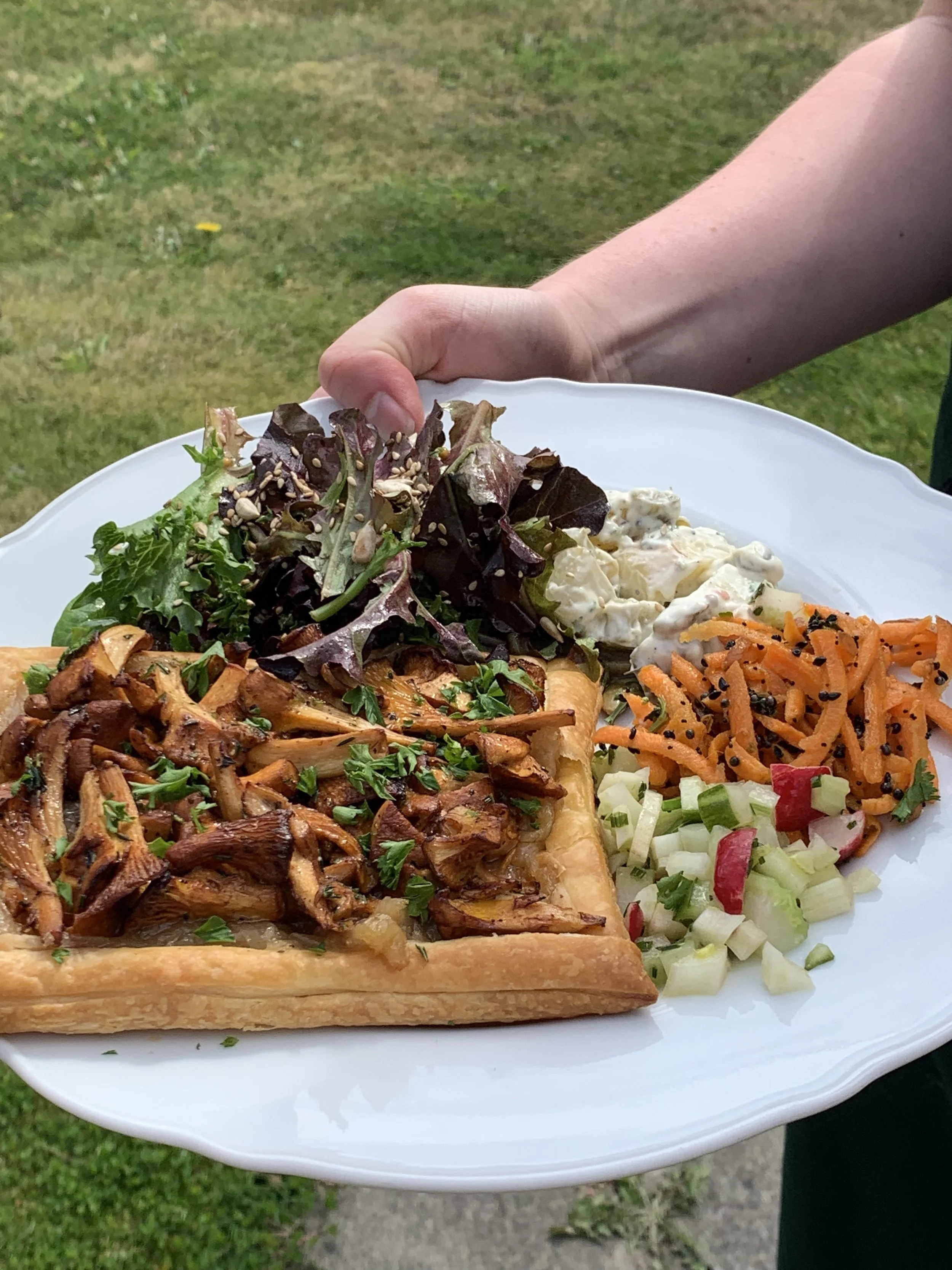 A chanterelle tart on a plate with salads, being held by a hand.