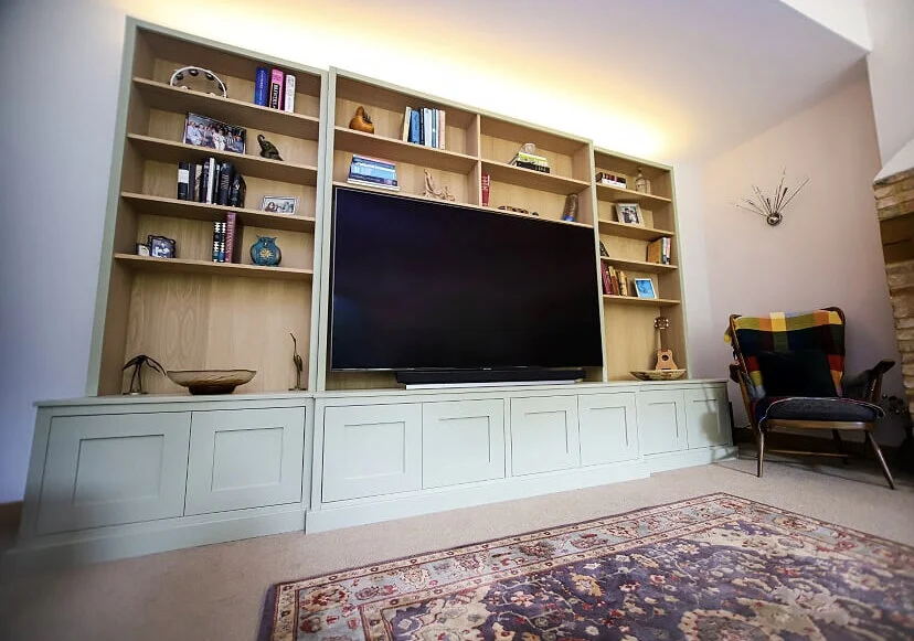 Living room with a large wooden bookshelf, a flat-screen TV, a colorful armchair, and a patterned rug.