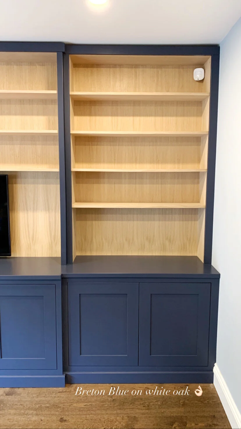 Empty built-in bookshelf with natural wood shelves and dark blue cabinets below, against a wall with a corner. Text overlay reading 'Breton Blue on white oak' with an OK hand emoji.