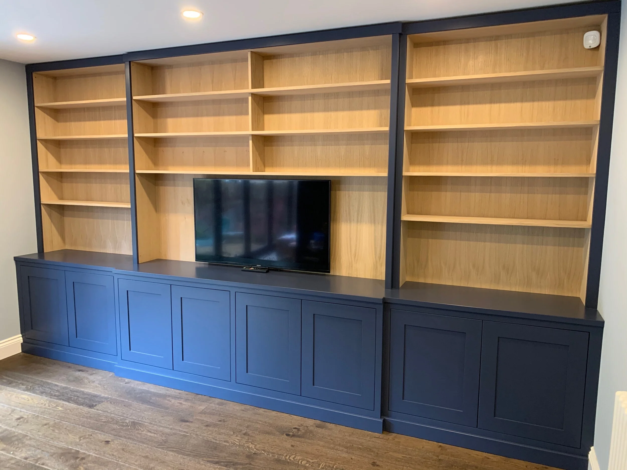 Empty wooden bookshelves with a TV in the center, set against a blue cabinet base, in a home or office room with wood flooring.