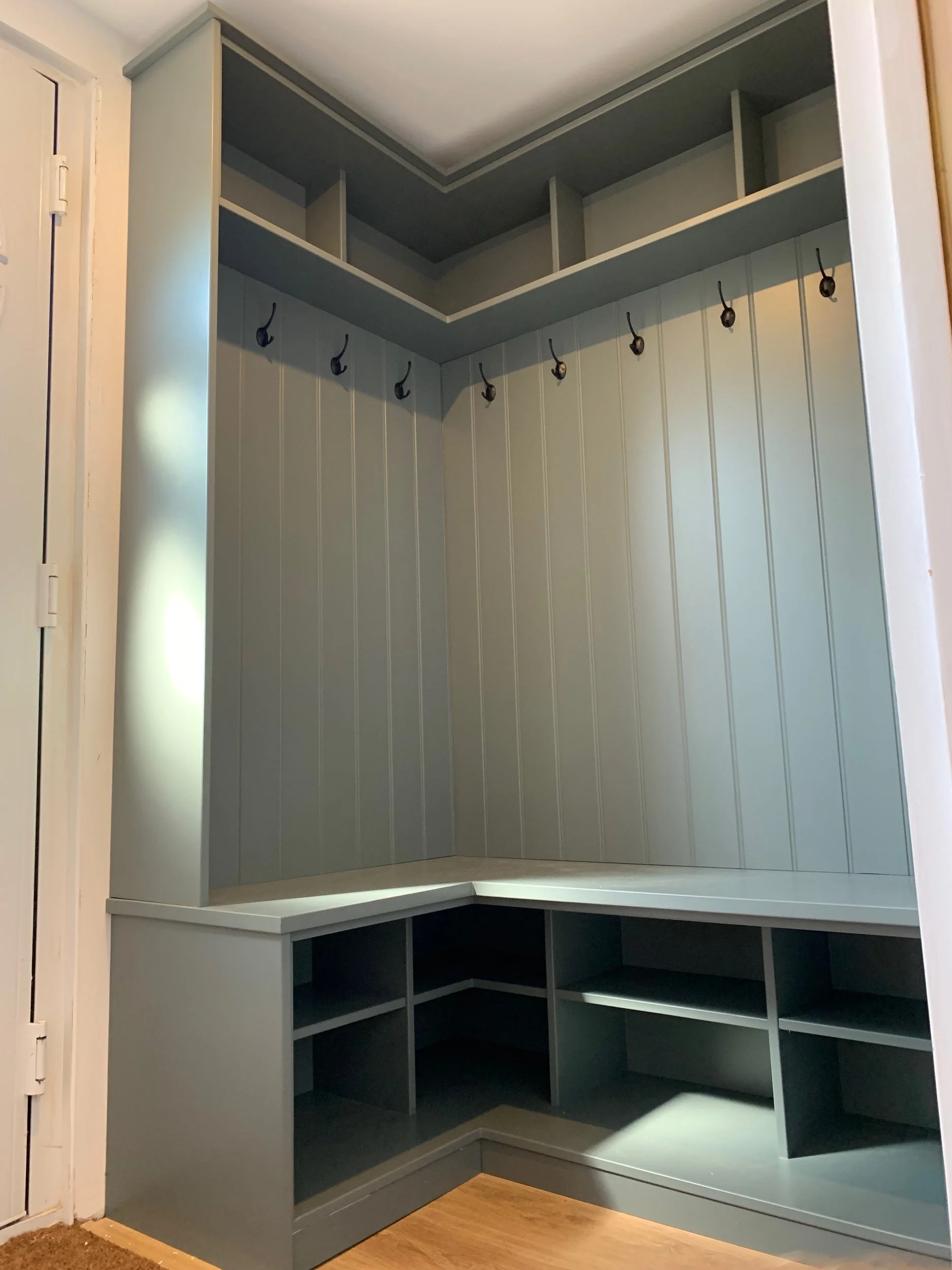 Gray built-in corner mudroom with hooks, open shelves, and cubbies.