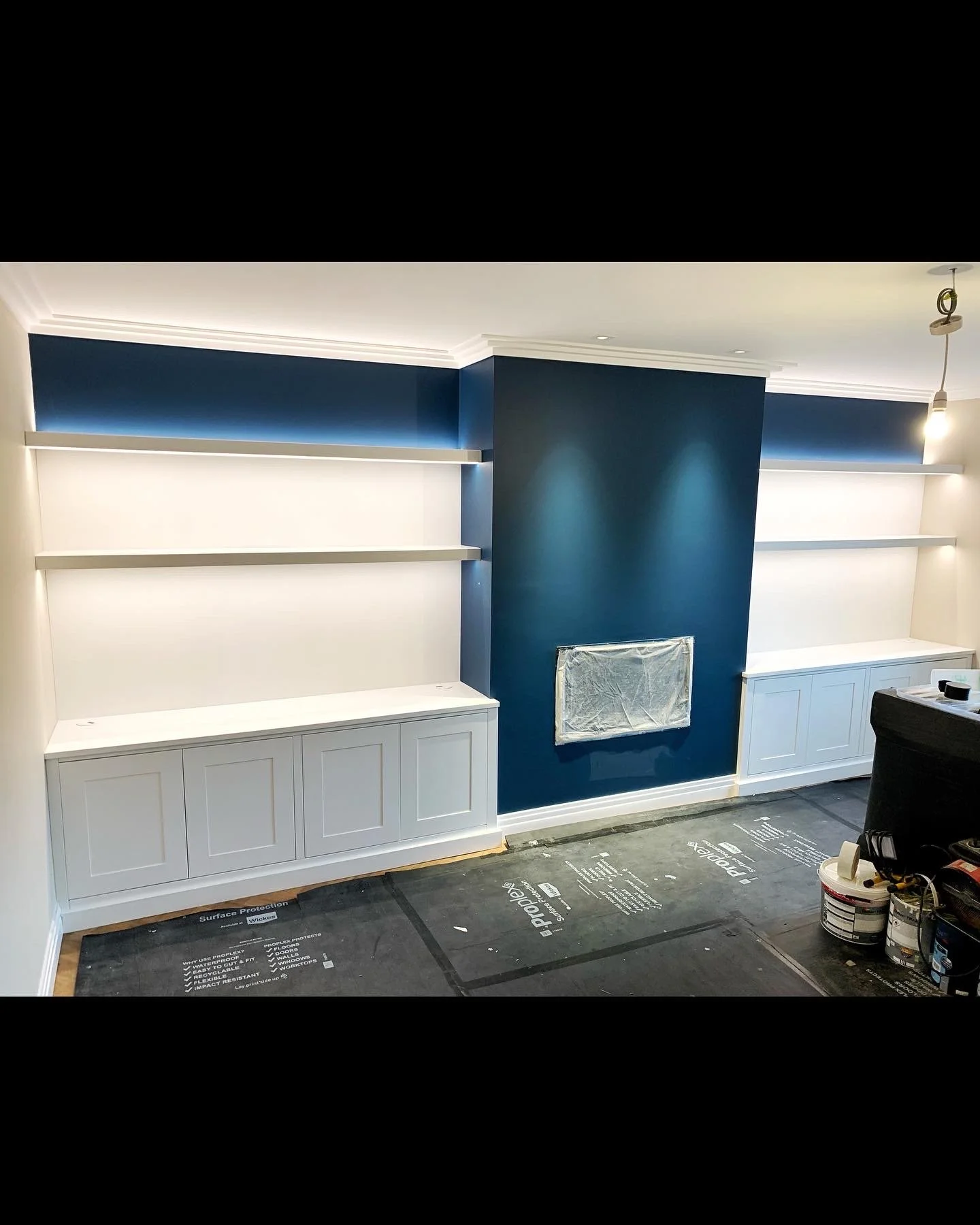 Living room with built-in shelves and cabinets, painted dark blue accent wall, under-construction with tools and materials on the floor.