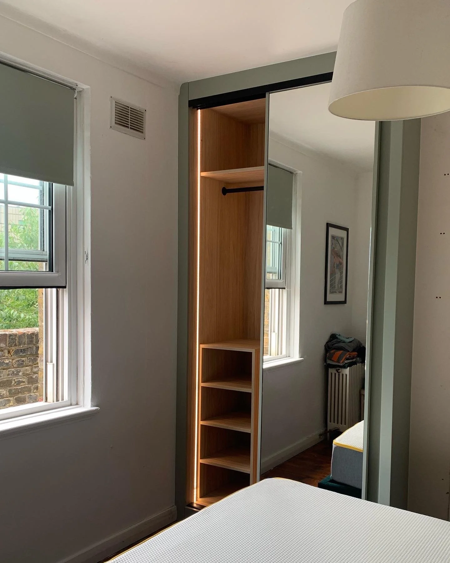 Built-in wardrobe with sliding mirrored doors, wooden shelves, and a hanging rod in a bedroom.